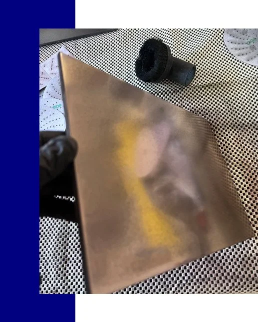 A person holding a reflective, metallic, square-shaped object, possibly a notebook or a box, with a black object on a dotted surface in the background.