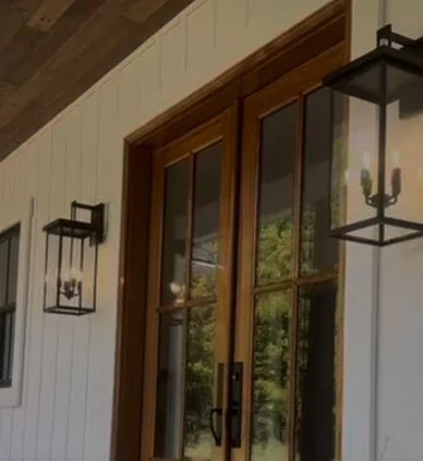Close-up of a wooden-framed window with two black lantern-style outdoor light fixtures on a white-paneled wall.