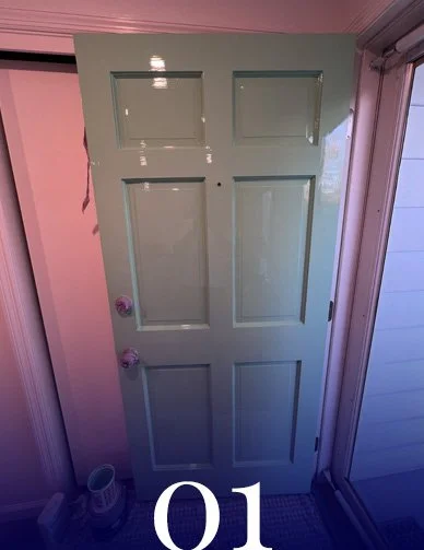 A light green interior door with six panels, slightly opened. The door has two doorknobs and is situated near a wall and a window, with a small container and a pair of shoes on the floor nearby.