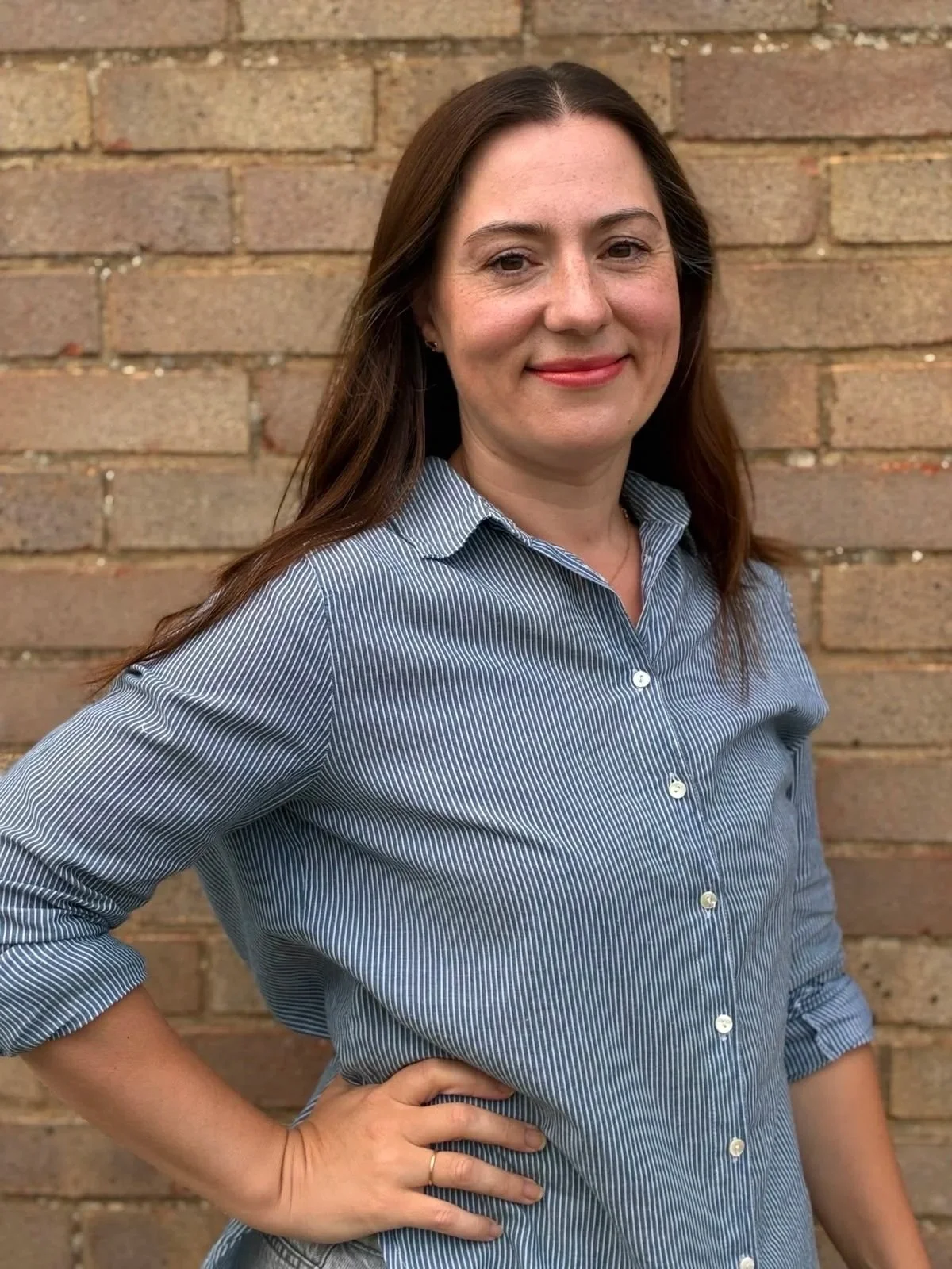 A white woman, in her 40s, with long dark brown hair in a blue shirt, smiling.
