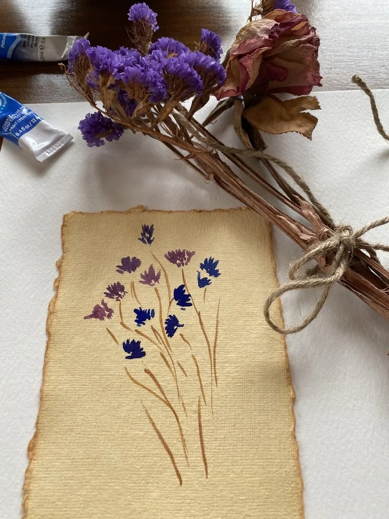 watercolour painting on deckled paper, of blue and purple wildlfowers with tied bundle of stems