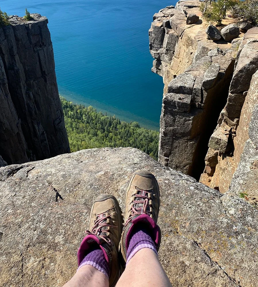 hiking boots of woman sitting down at edge of cliff overlooking rock formations and Lake Superior
