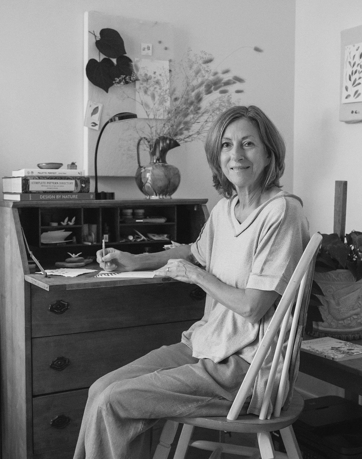 black and white image of woman, Dale Bialis at her desk, drawing and looking at camera