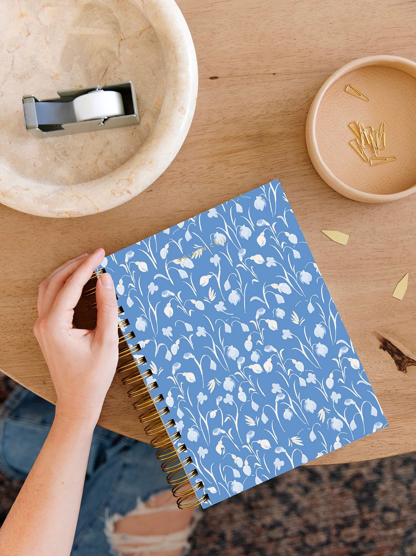 coil notebook with white flower pattern on a blue background on a table with stationery supplies
