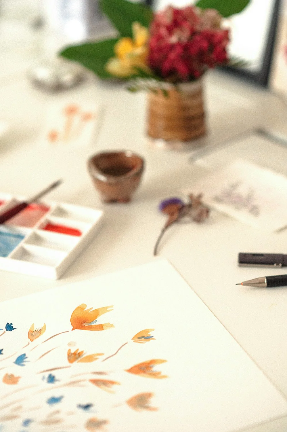 watercolour flower painting on desk with art supplies and flowers in a vase