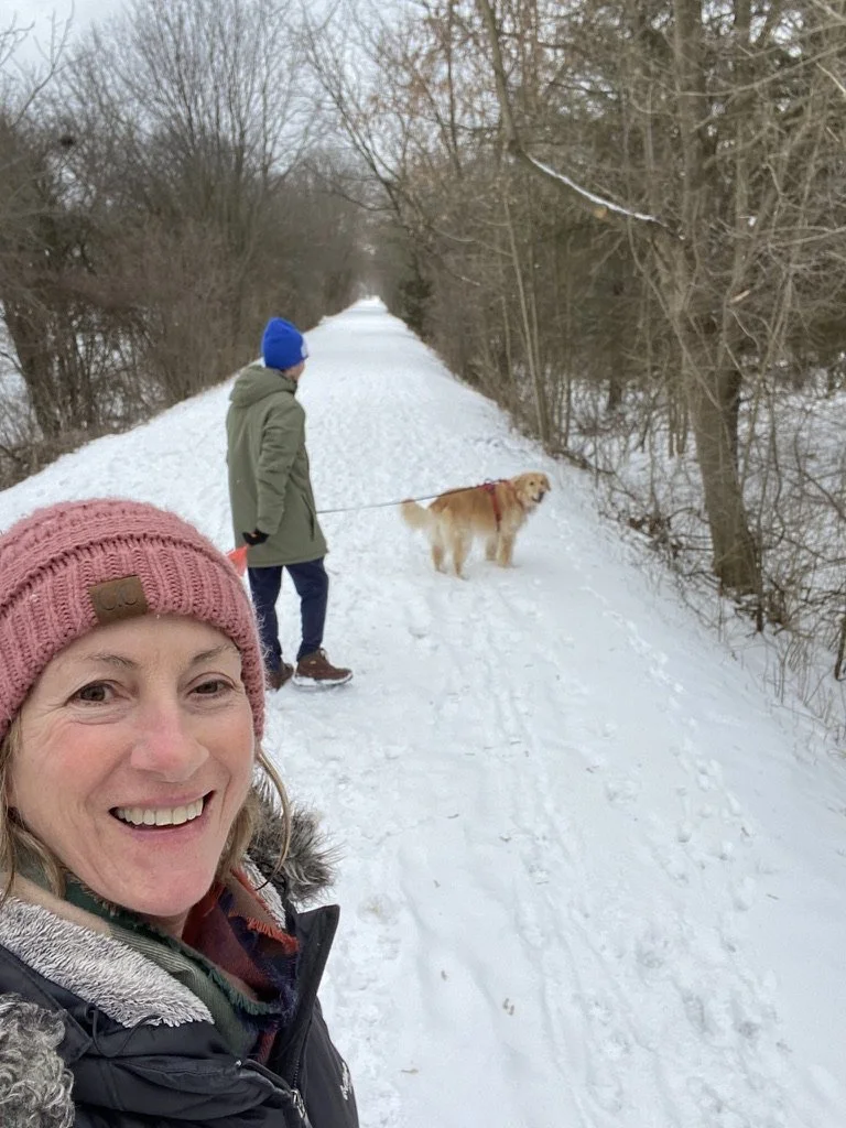 two people, woman and man, walking dog on snow trail, woman taking selfie