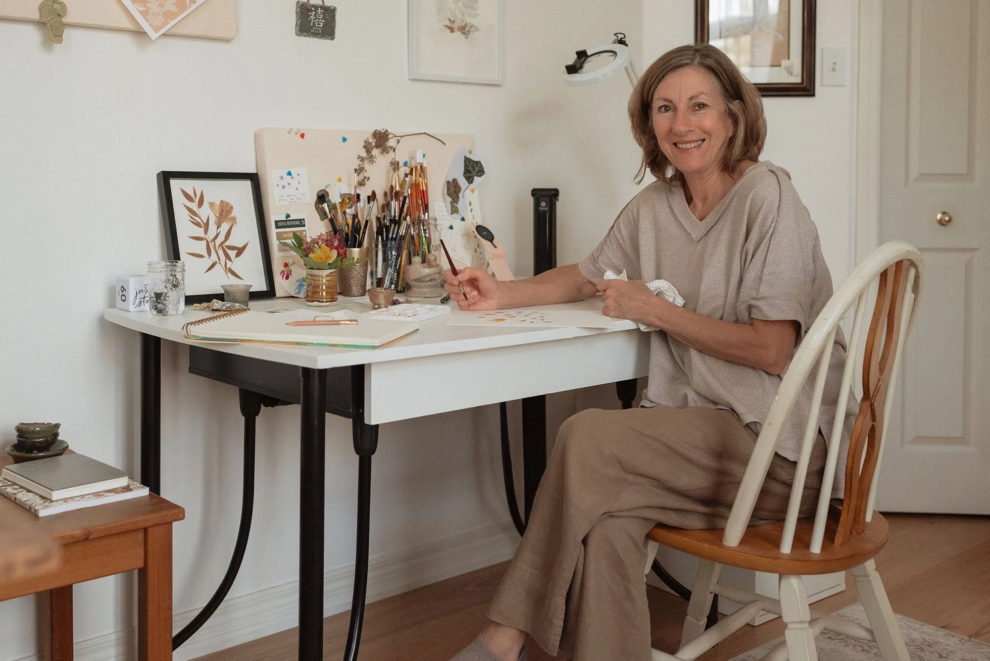 smiling woman, Dale Bialas, sitting at desk painting watercolour flowers