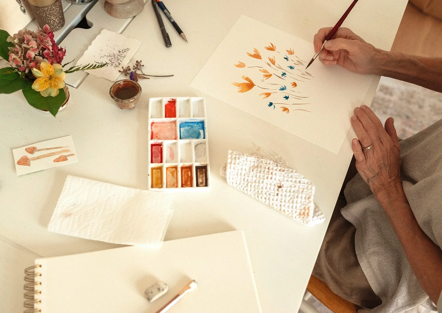 overhead view of woman painting watercolour flowers on desk