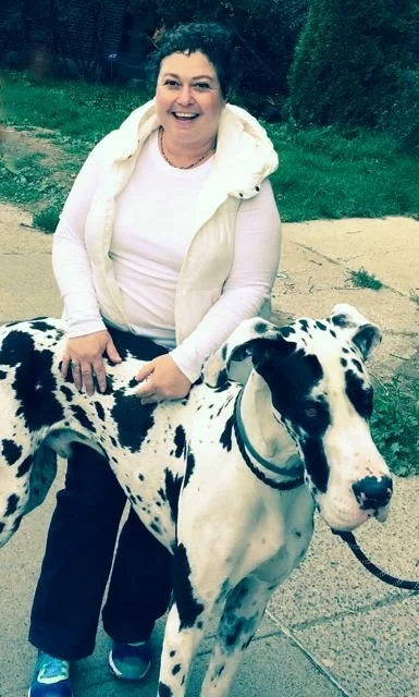 A woman smiling outdoors with her Dalmatian dog on a leash.
