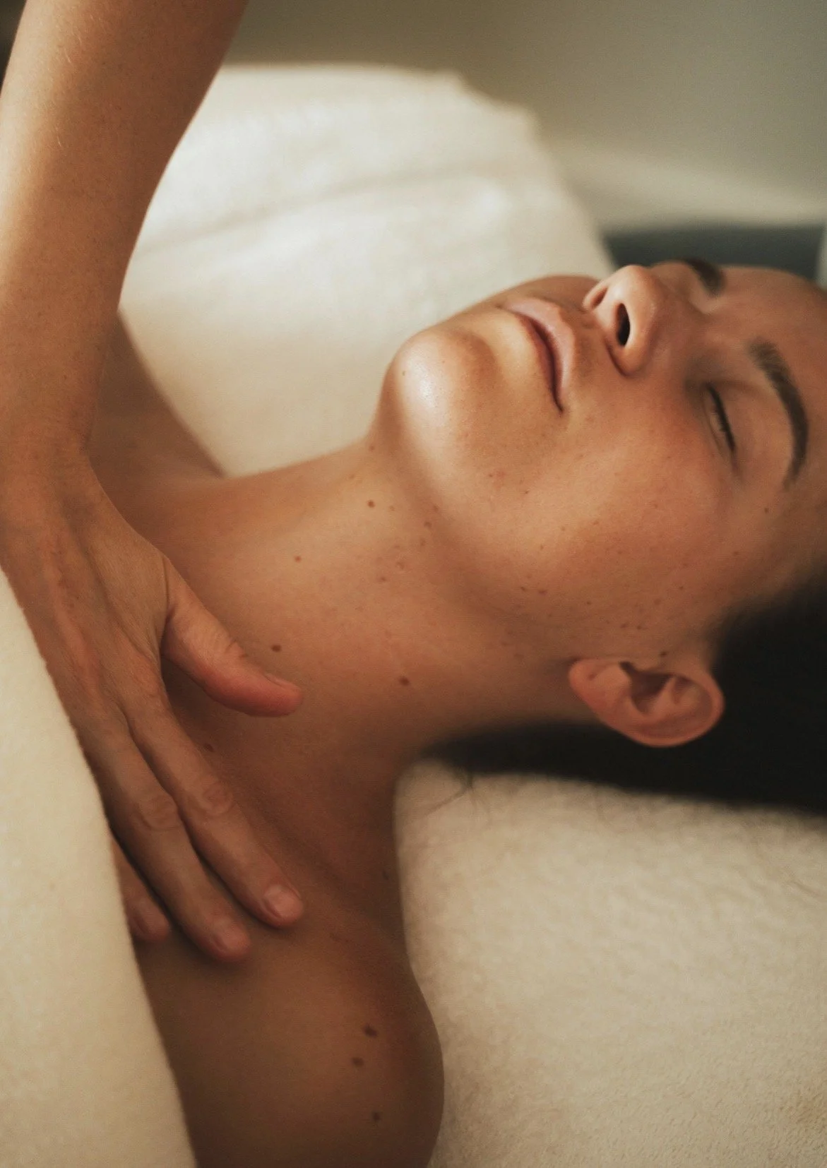 A woman receiving a massage in a spa setting, with her eyes closed and a relaxed expression.