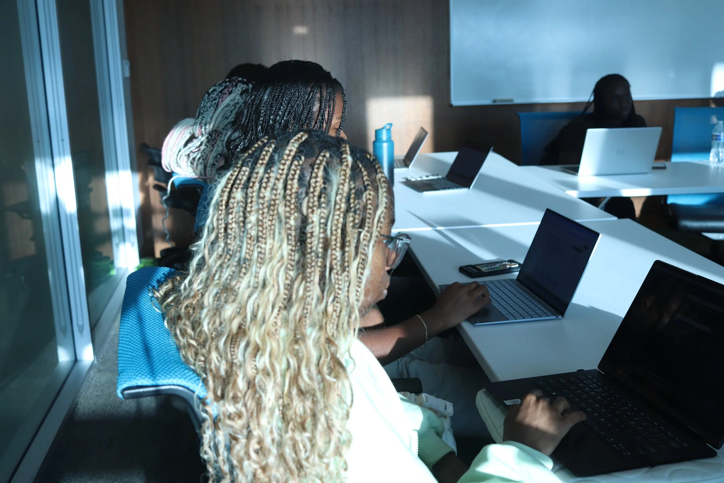 People sitting at a table using laptops in a classroom or meeting setting.