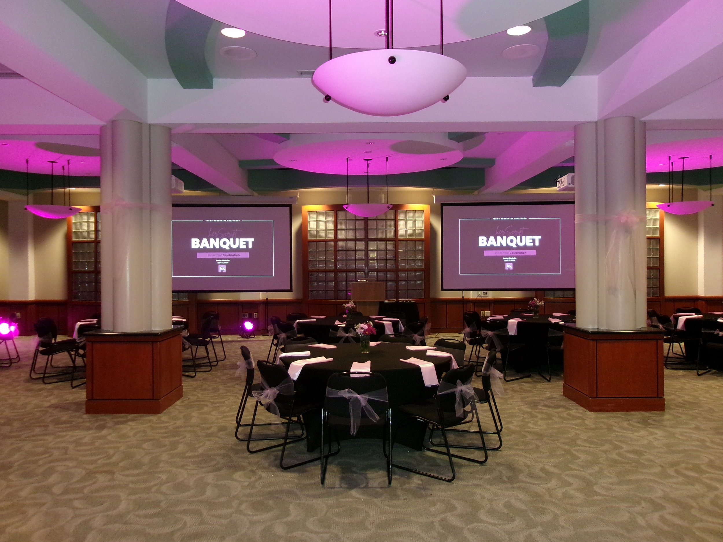 Event hall set up for a banquet with round tables, chairs, and a large projector screen.
