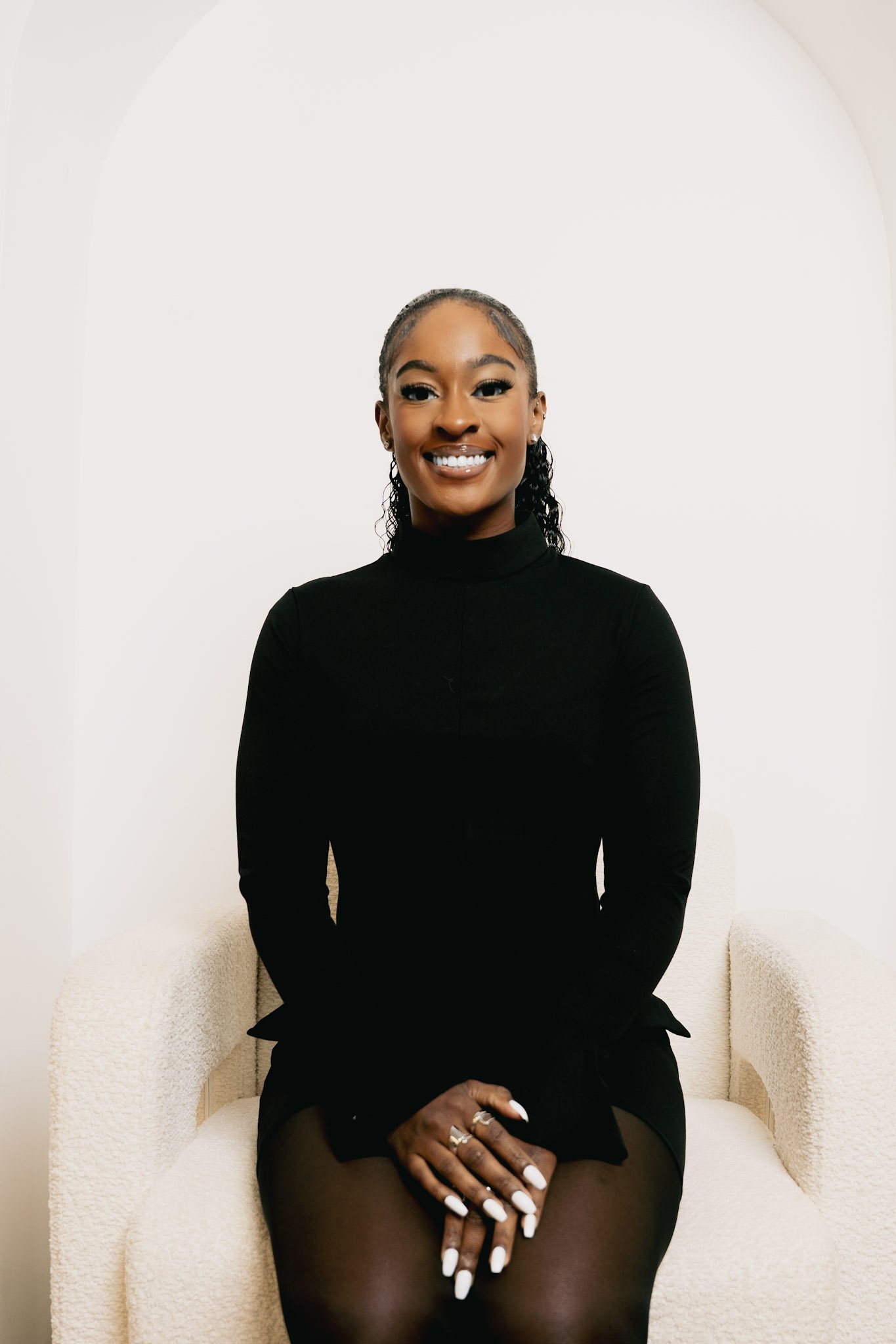 Person in a beige suit with crossed arms smiling indoors.