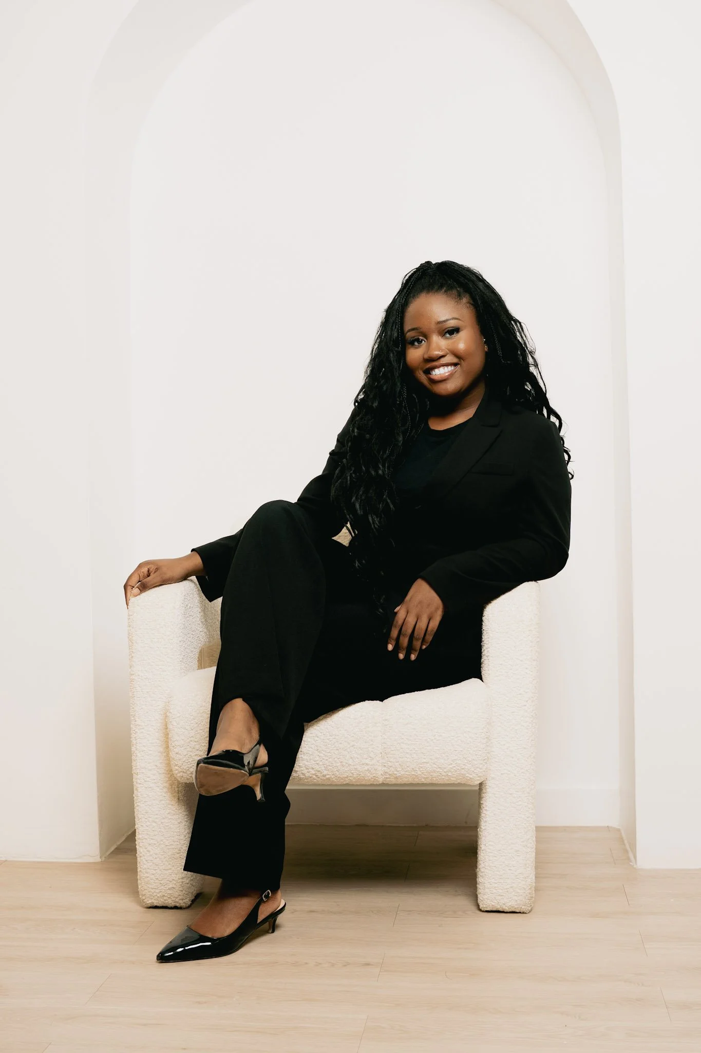 Person with glasses and braided hair wearing a light pink blazer, smiling in a professional setting.