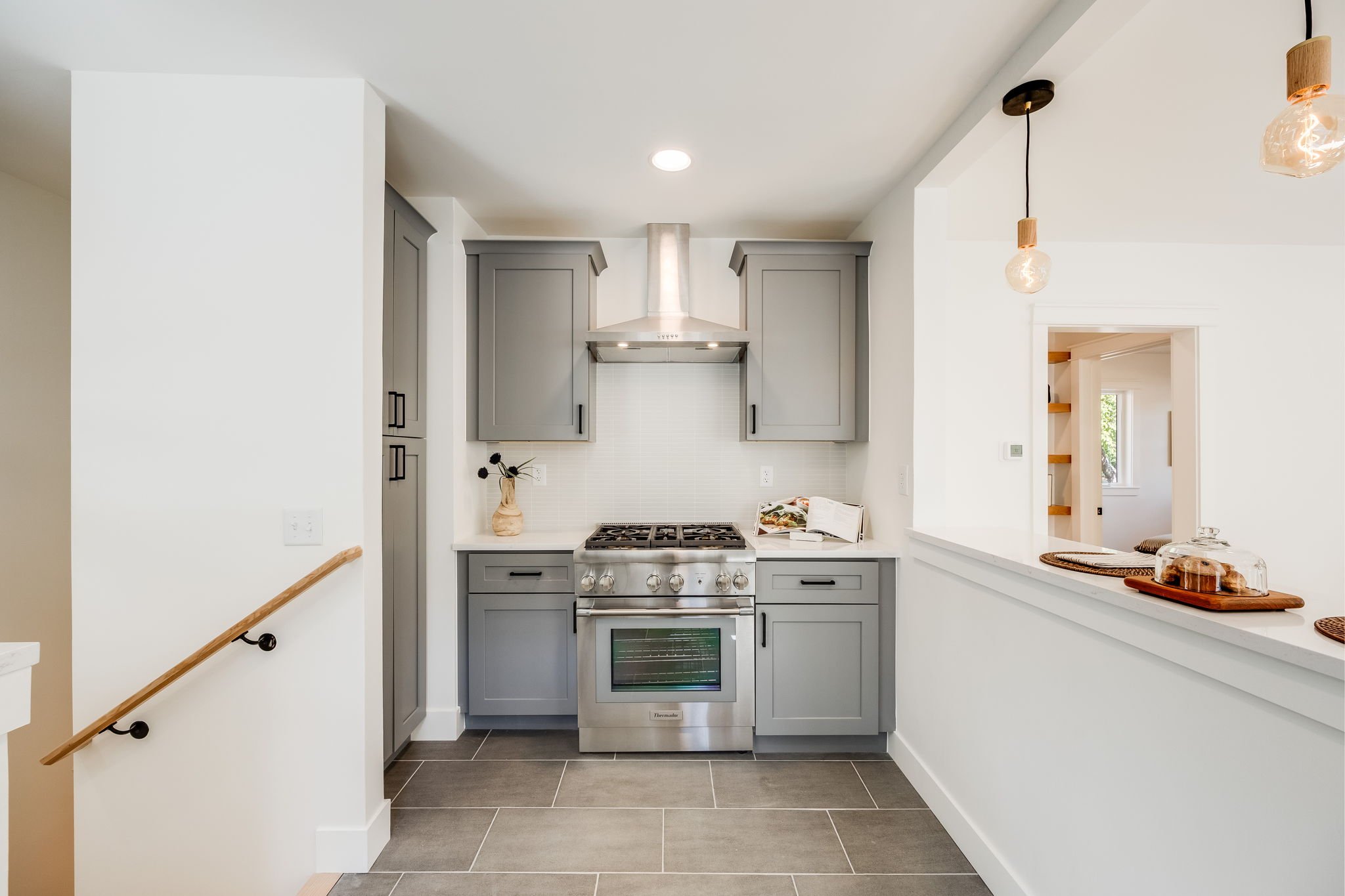 Modern kitchen with gray cabinets, stainless steel stove, white backsplash, and pendant lights.