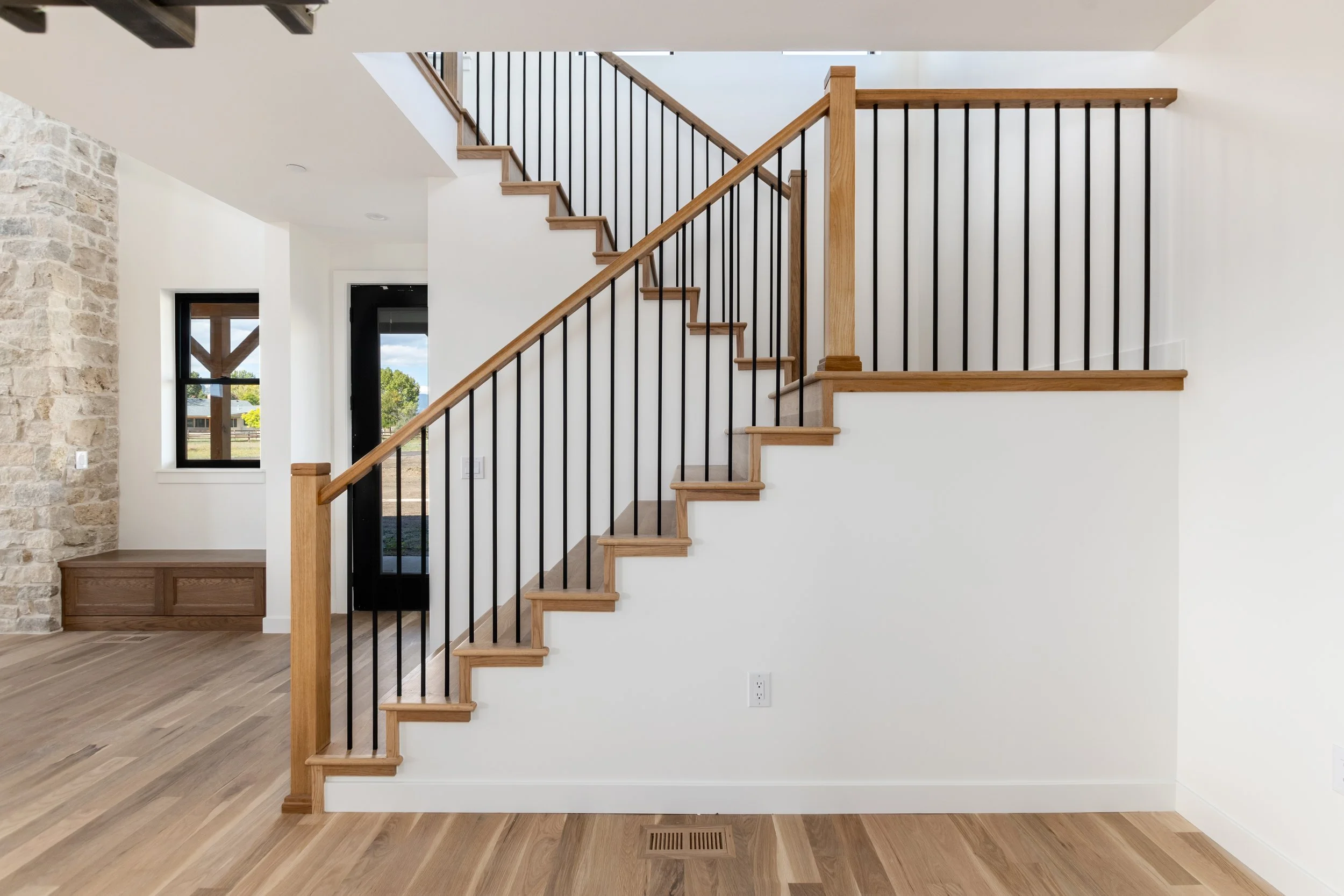 Interior view of a modern staircase with wooden steps and black metal railings inside a house.