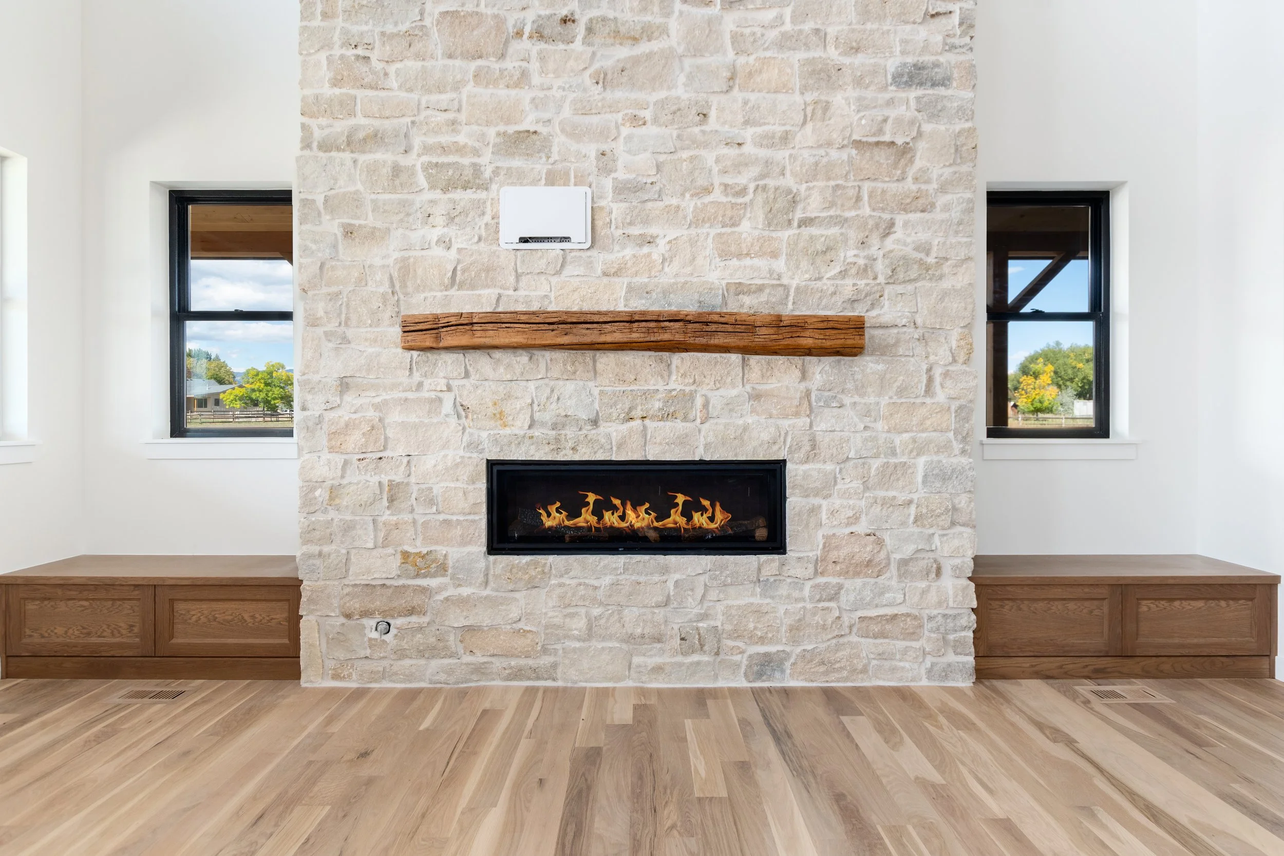 Living room with a stone fireplace, two small windows on either side, and wooden built-in benches.