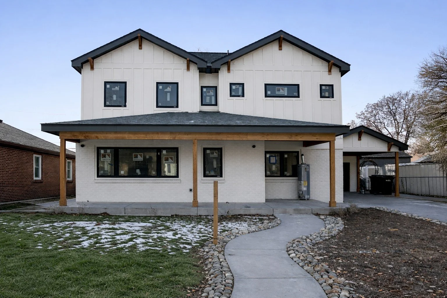 New two-story house under construction with a white exterior, dark roof, and large front windows, with a curved walkway and partially landscaped yard.