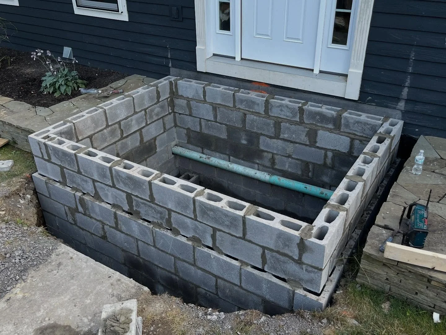 Part one of a multi-phase project for a homeowner looking to add a concrete porch to complement their stone and hardscape-focused exterior. After excavation, we poured a reinforced footer and constructed a block foundation. Each block core was fully 
