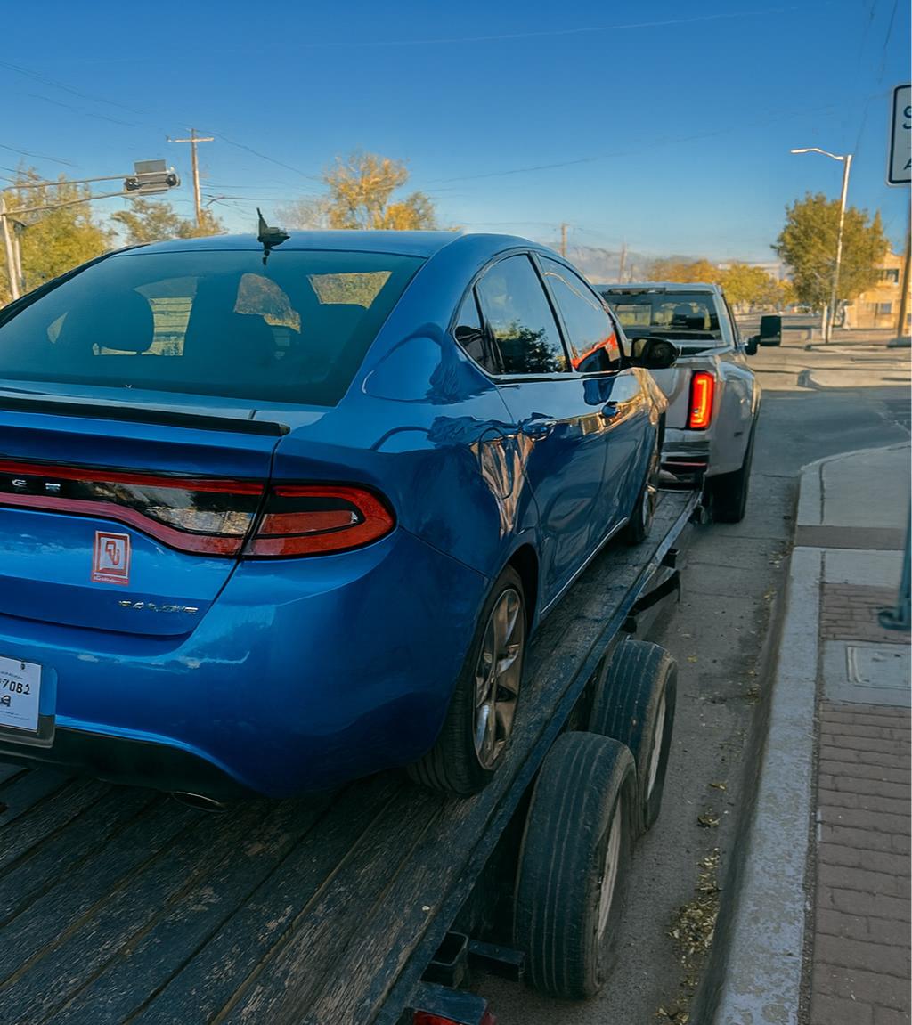Blue sedan on a flatbed tow truck, parked on the side of the street.