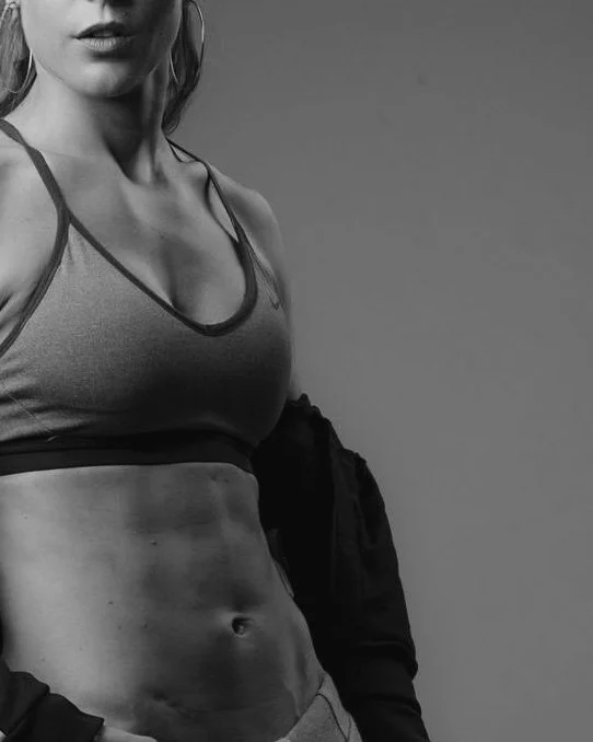Photo en noir et blanc d'une femme sportive en débardeur, montrant son abdomen tonique.