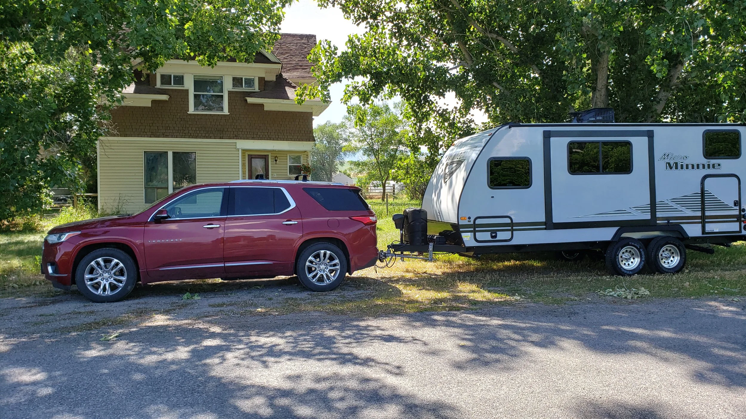 Red SUV towing a white travel trailer parked on a residential street with trees and a house in the background.