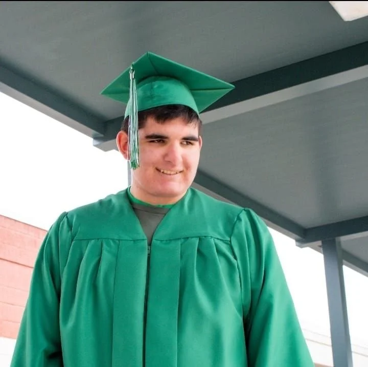 A young man in a green graduation gown and cap smiling outdoors.