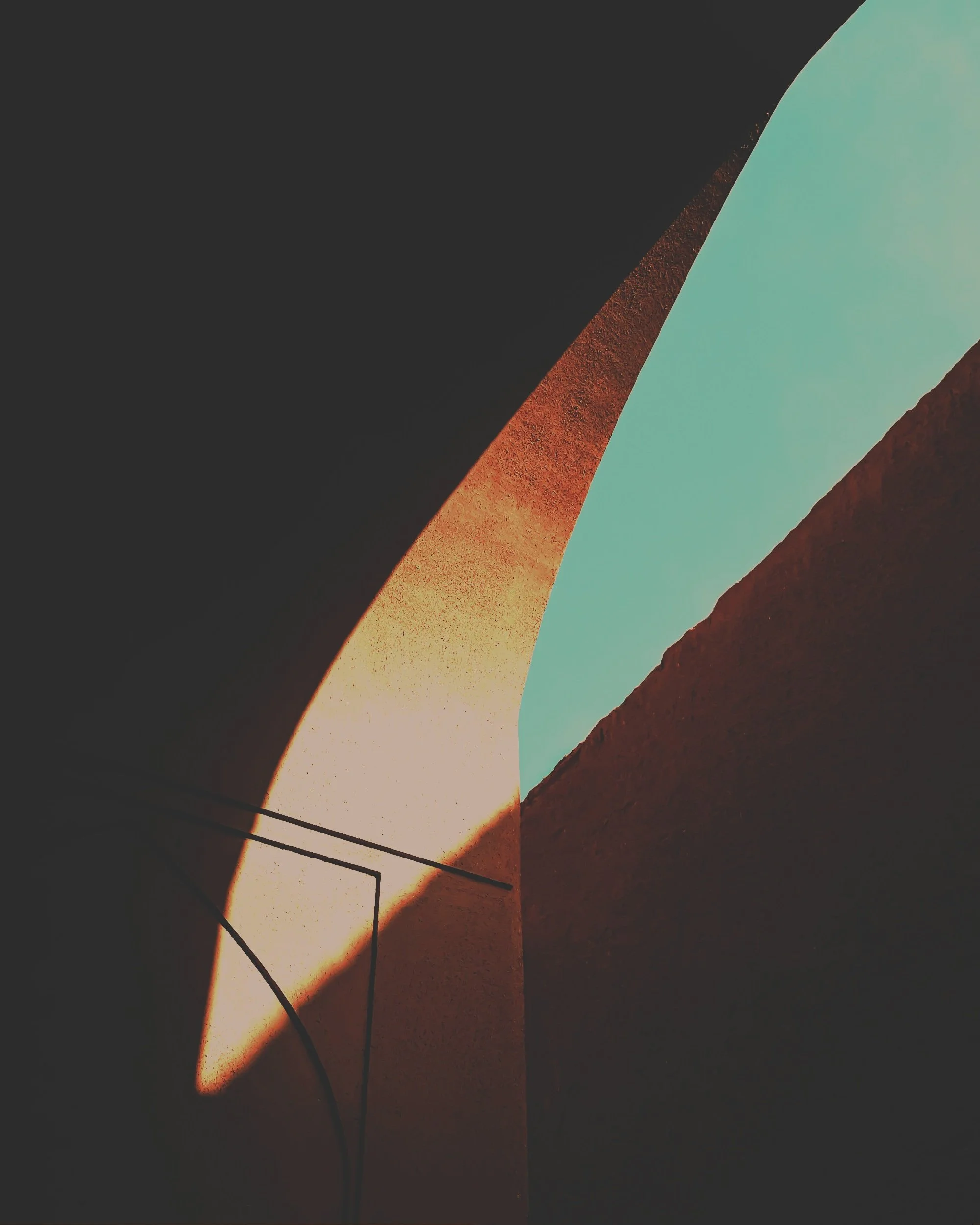 An abstract architectural image showing only a portion of an archway and the wall behind it and a sliver of sky amongst the shadows that looks like an eye. Middle Frequency.