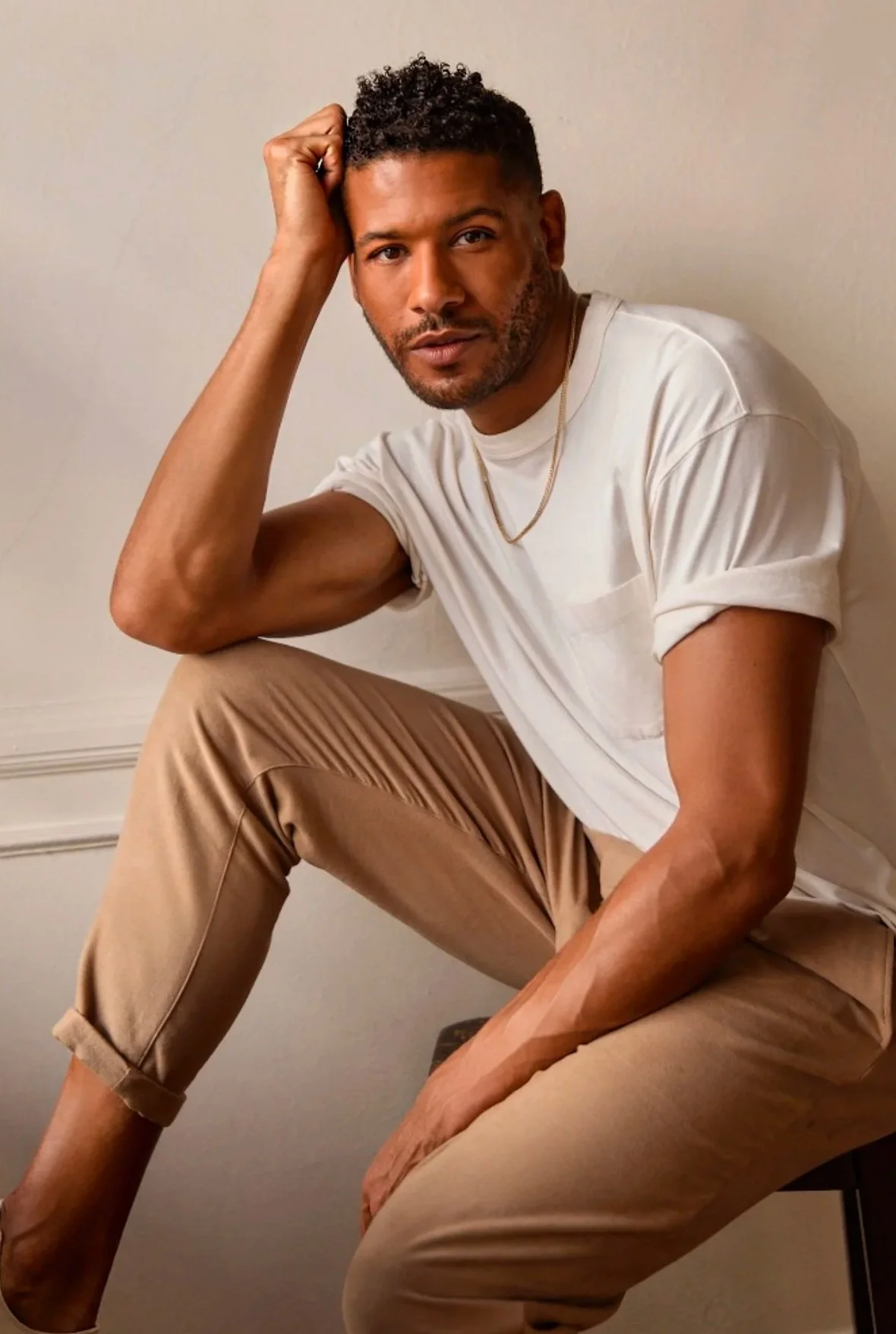 A man named Jeffrey Bowyer-Chapman sitting on a stool with one leg bent, resting his elbow on his knee and his head on his hand. Middle Frequency.