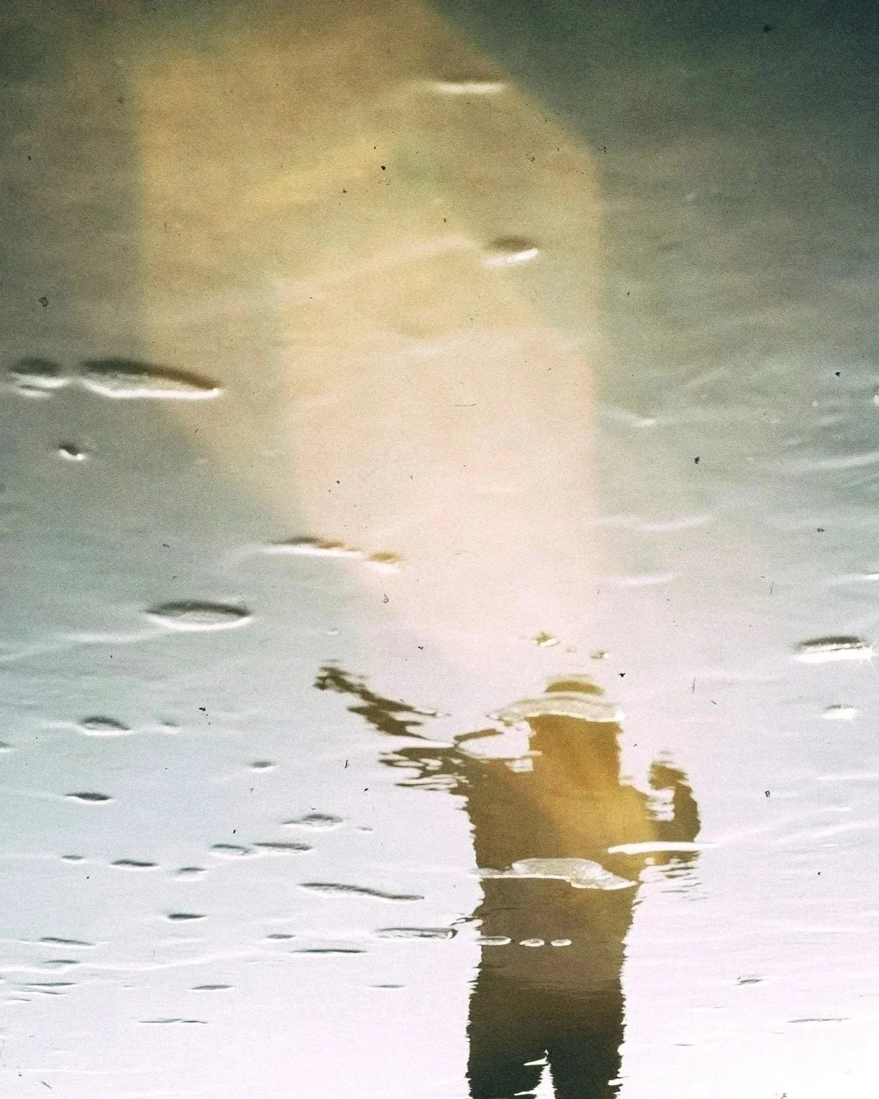 A reflection in water of a person with one arm raised up and the other arm pulled back in a super hero pose with a diamond-shaped light beam above their head. Middle Frequency.
