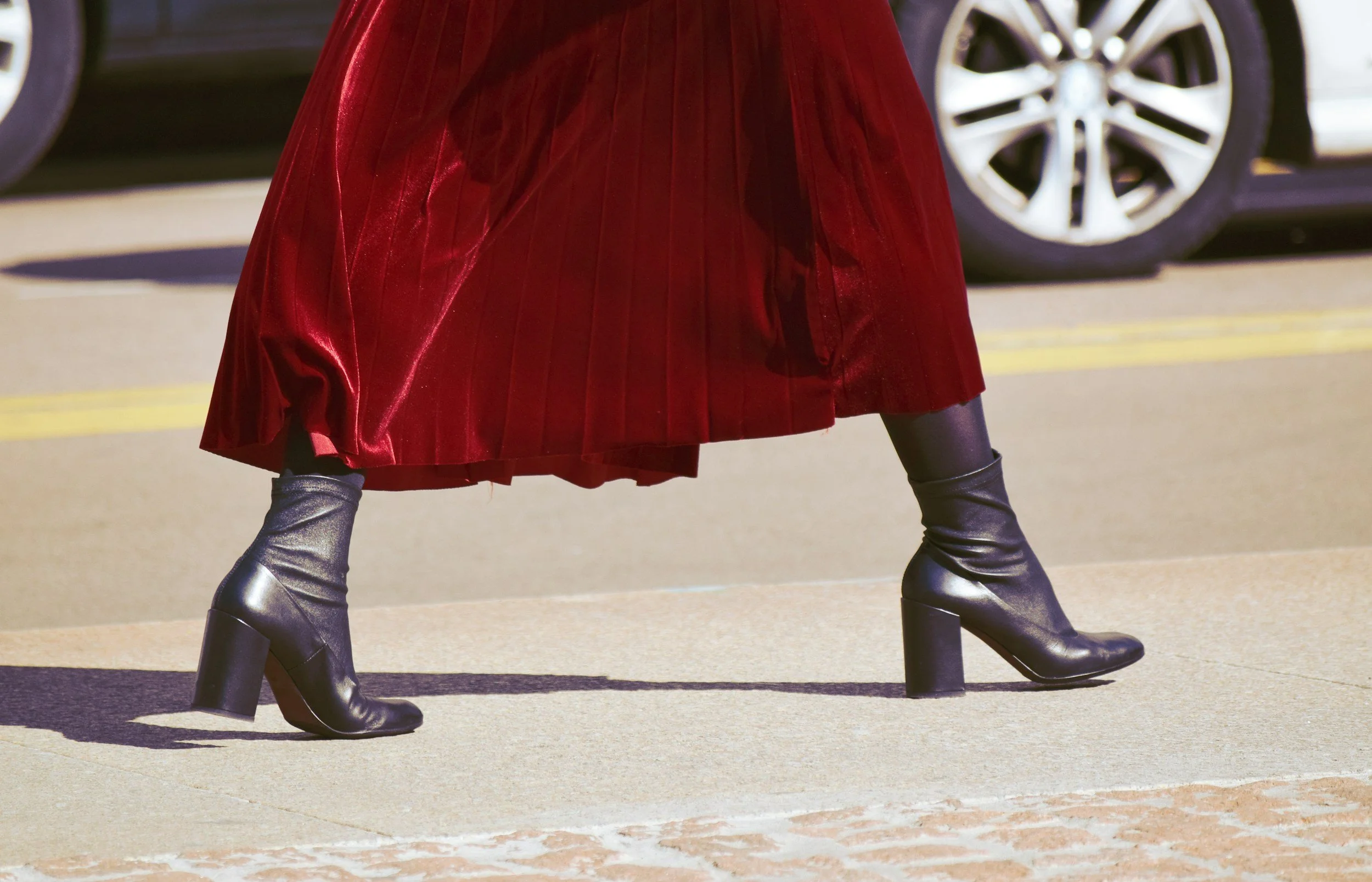 Person walking in black heels and a red velvet skirt, with cars in the background