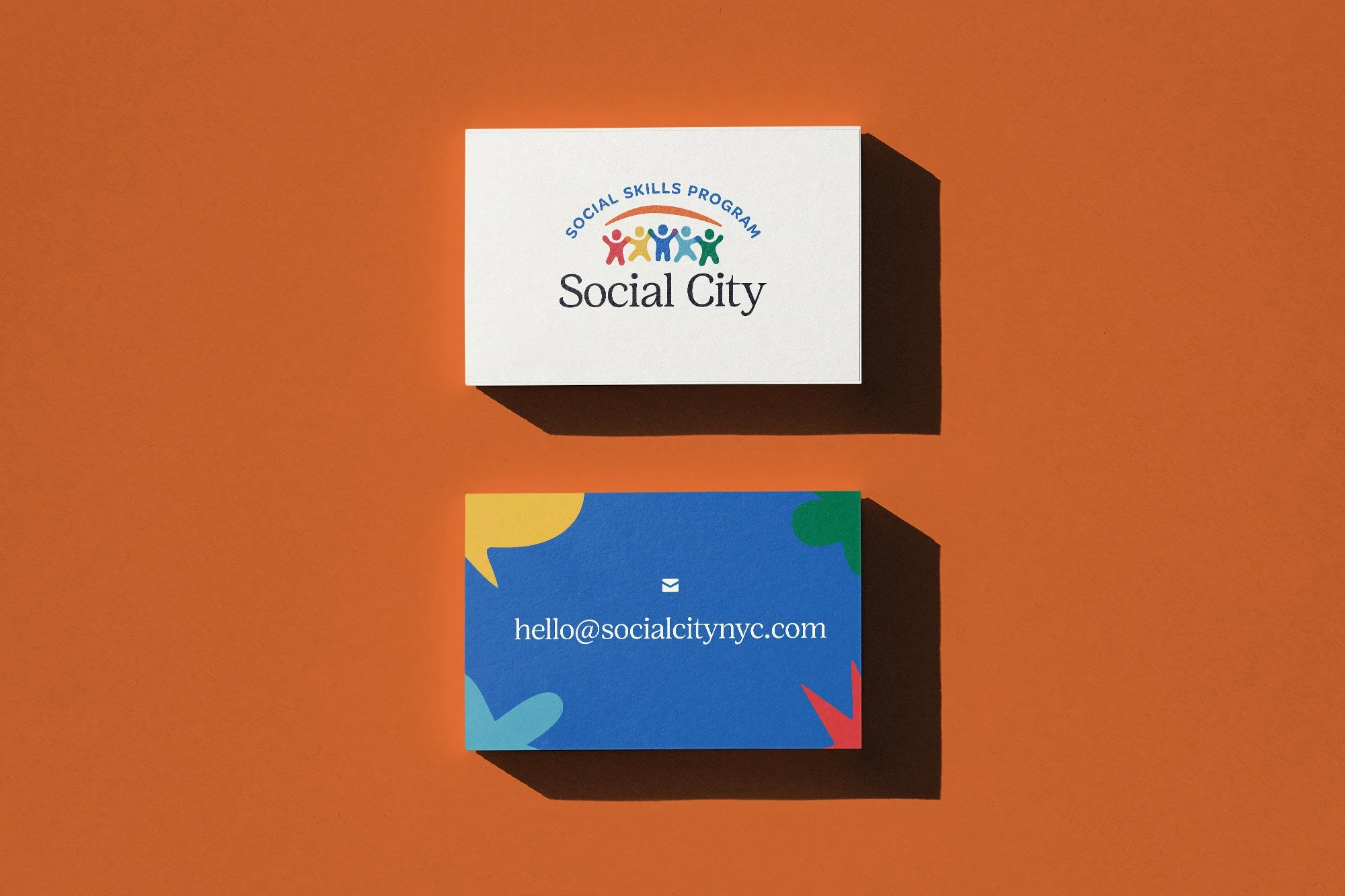 Business cards for Social City, a social skills program. The top card has a white background with the logo and text, and the bottom card is blue with colorful abstract shapes and the email hello@socialcitynyc.com.