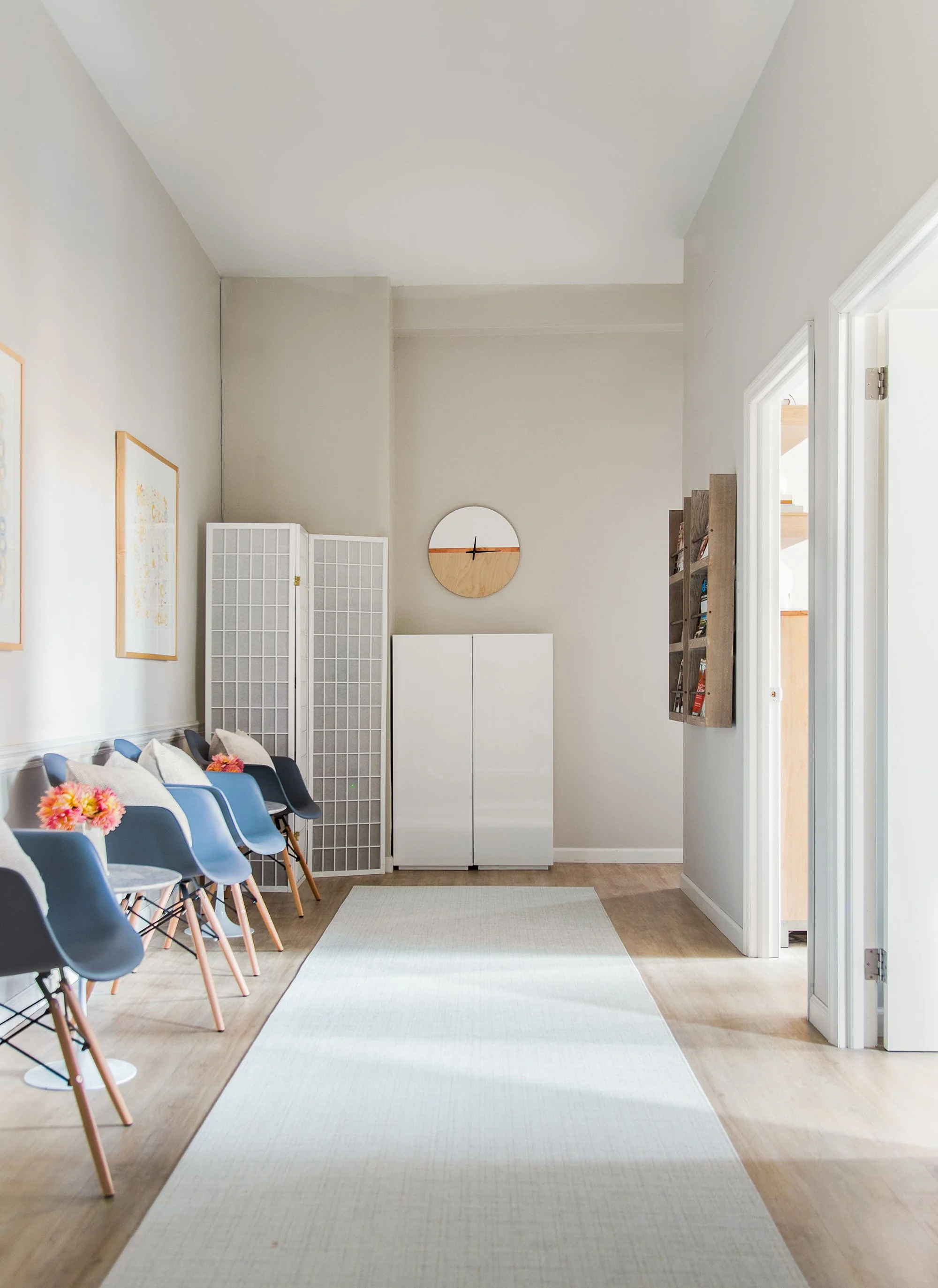 Waiting room with chairs, artwork, a folding screen, a clock, and a cabinet.