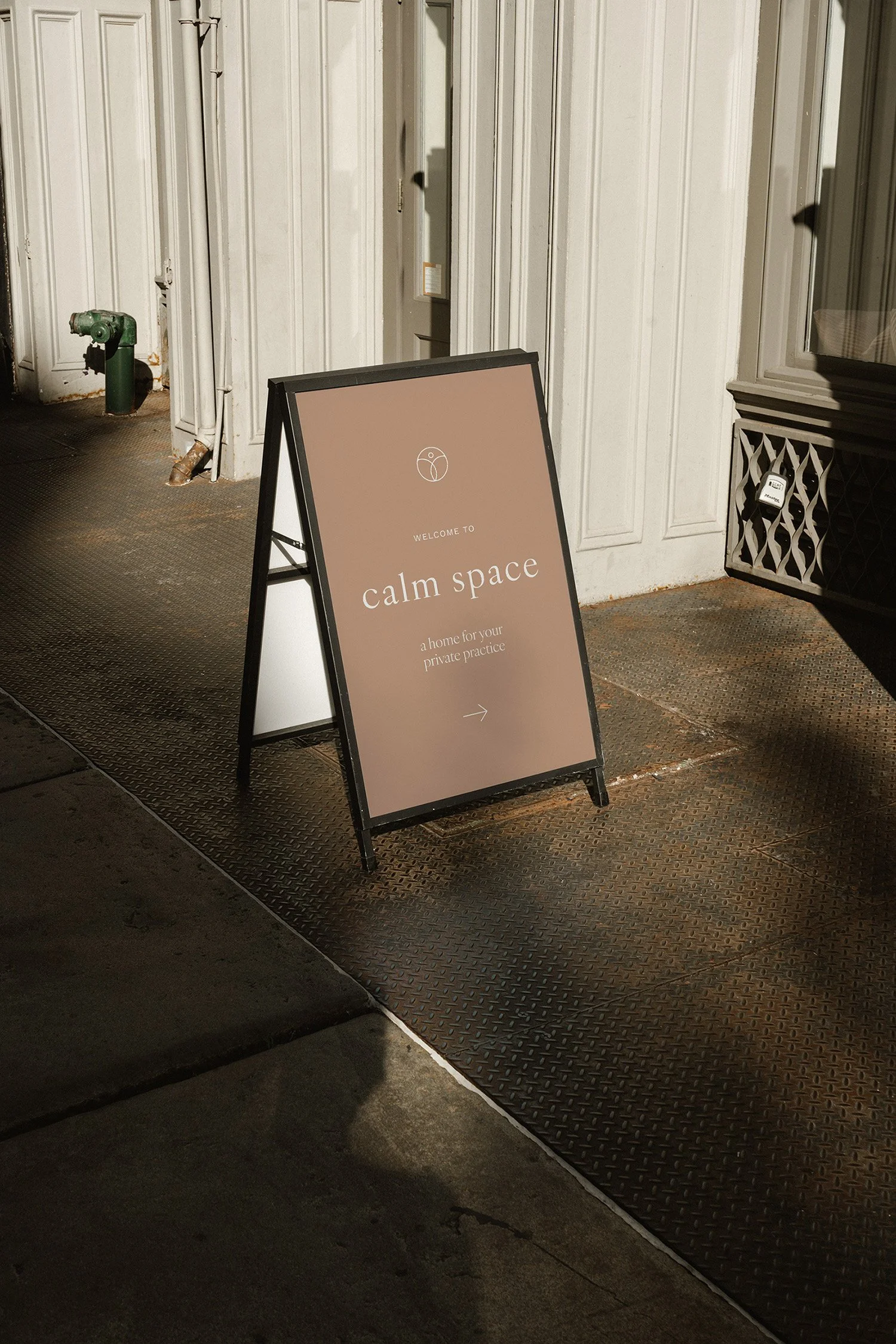 A sidewalk sign for 'calm space,' a home for private practice, with a minimalist design on a brown background and an arrow pointing right.