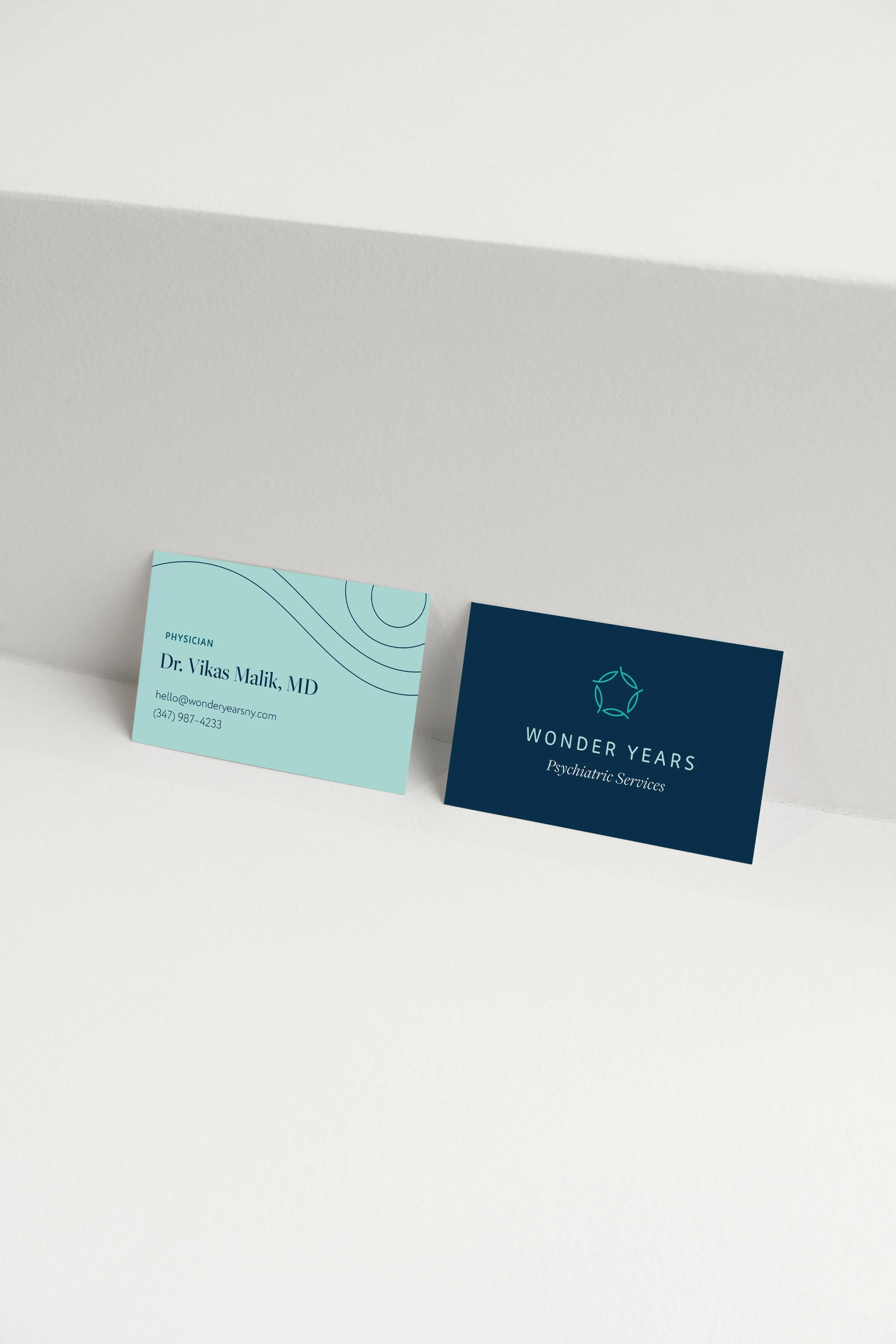 Two business cards on a white surface, one for Dr. Vikas Malik, MD, and the other for Wonder Years Psychiatric Services.