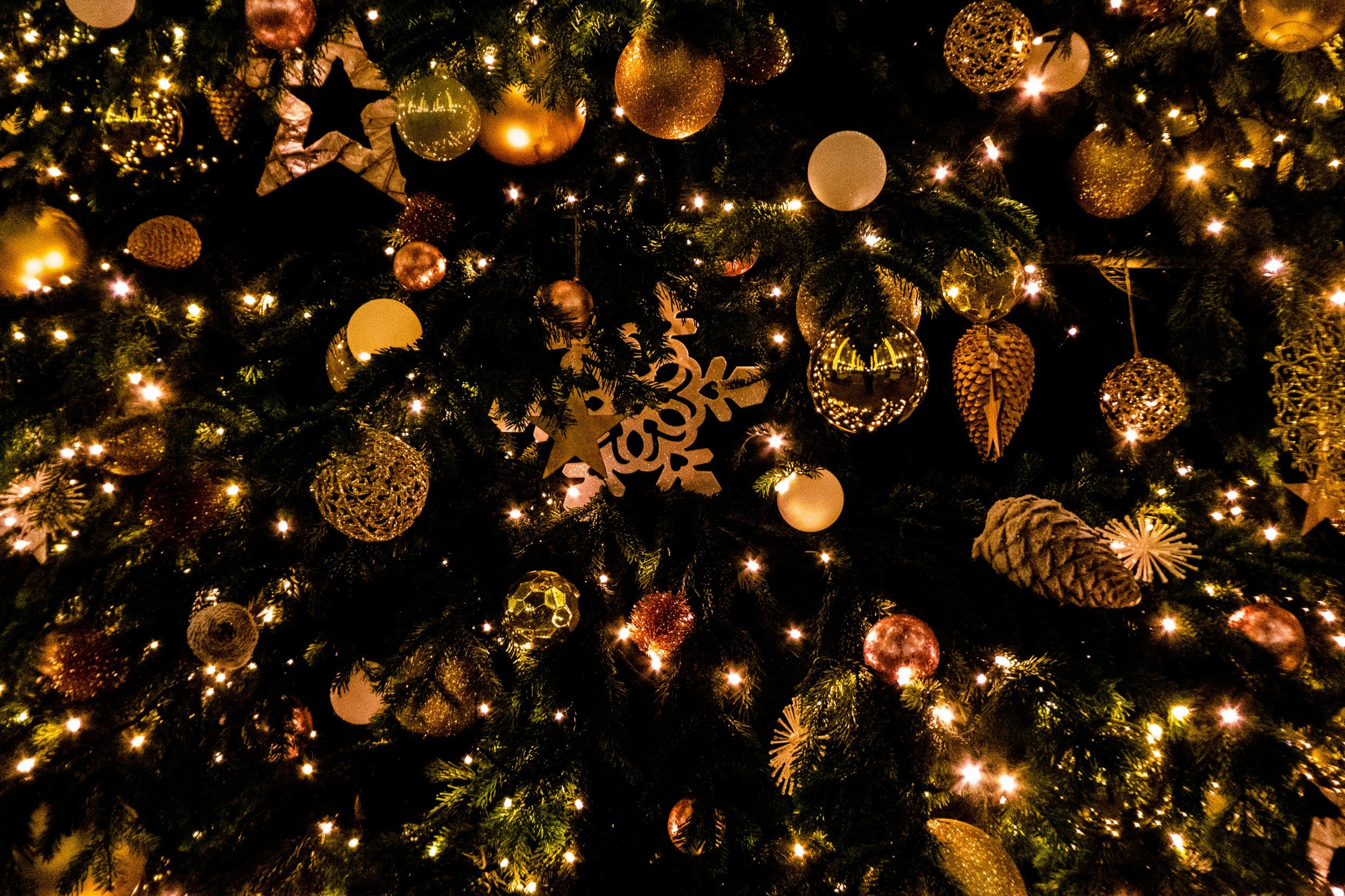 Close-up of a decorated Christmas tree with gold and white ornaments, pinecones, snowflakes, and string lights.