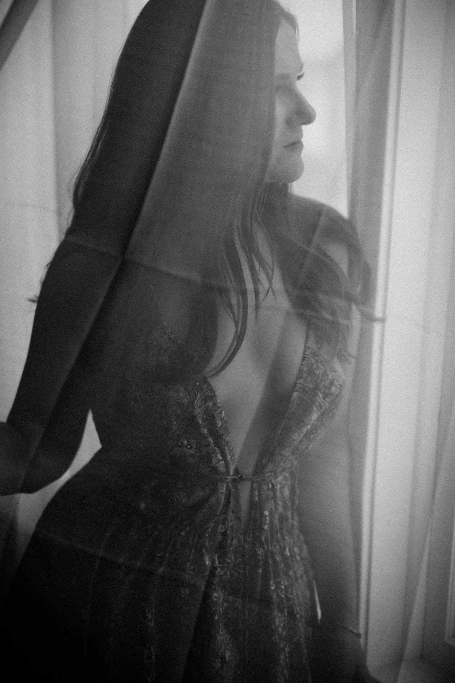Emm with long hair looking out a window, seen through a glass pane, in black and white.