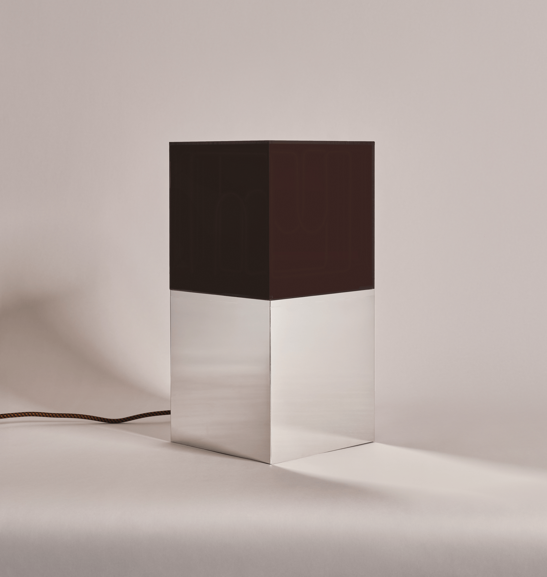 A modern neon sculpture lamp with a black top and silver base, connected to a braided electrical cord, placed on a plain white background.