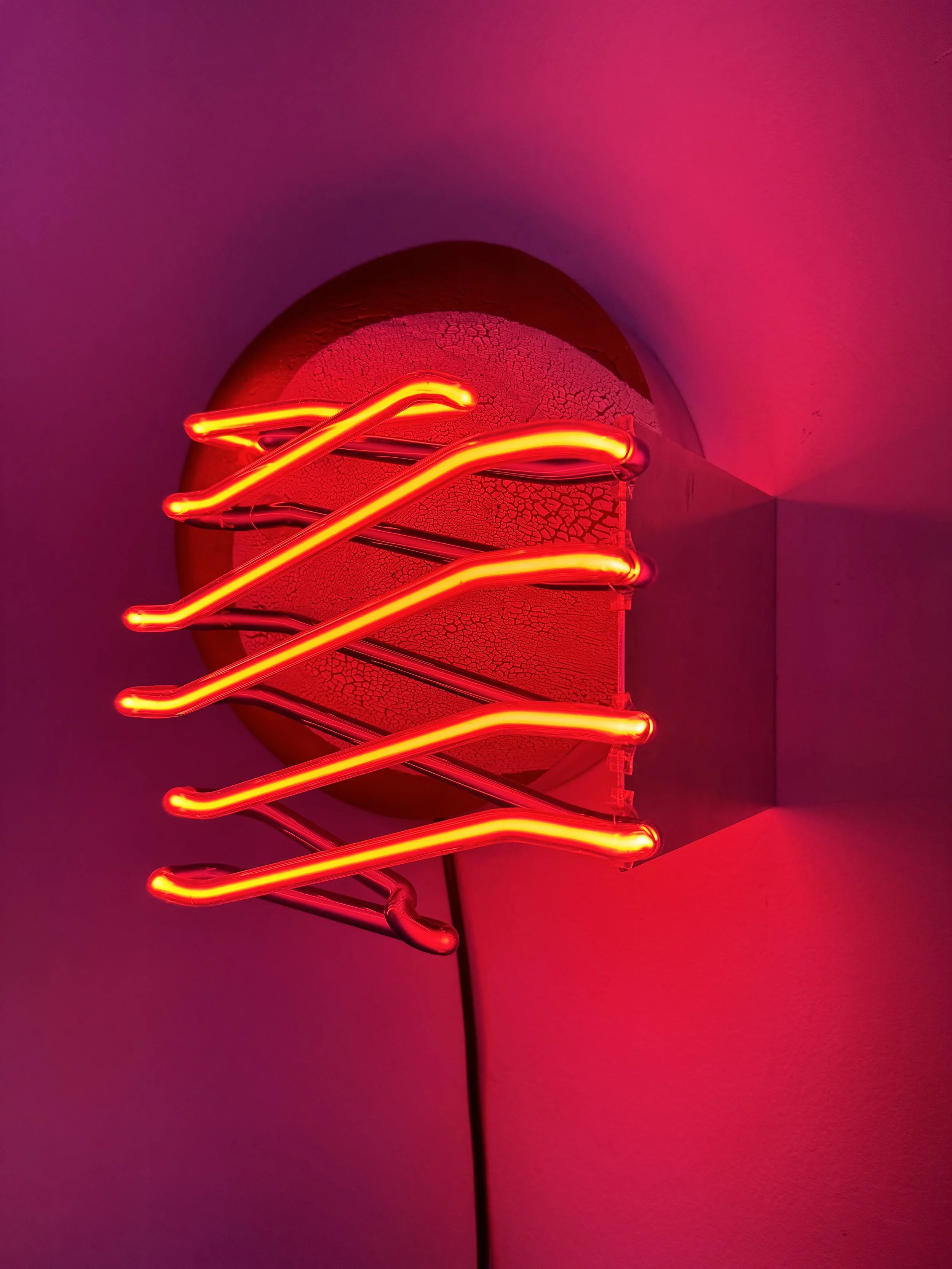 Close-up of a red neon light fixture mounted on a wall, with a cracked, textured surface background.