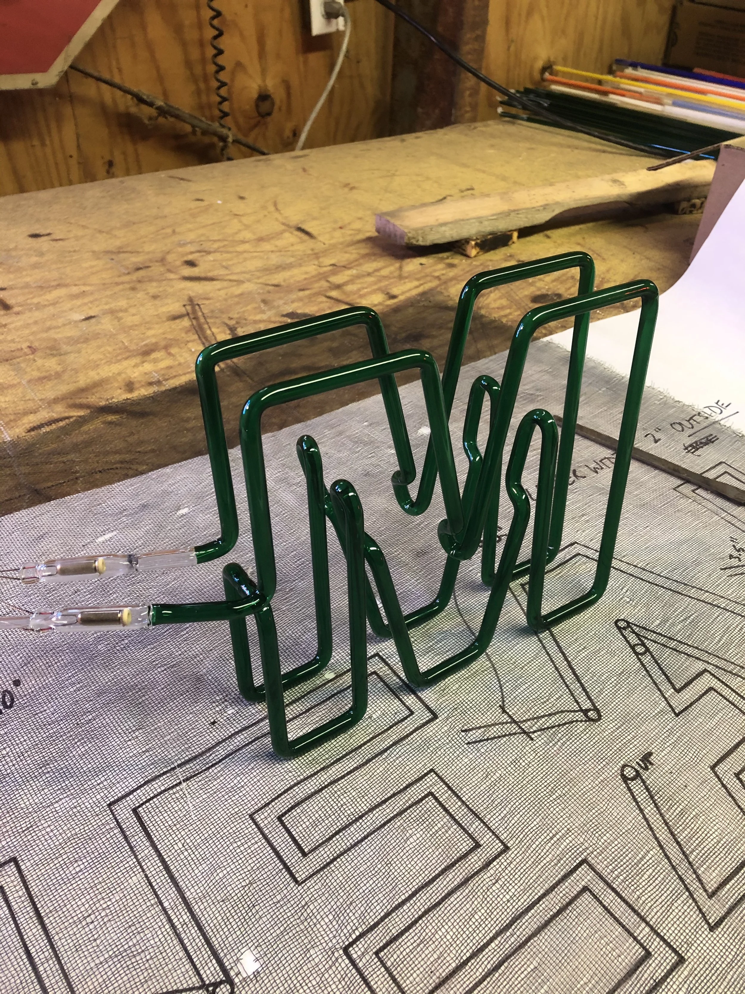 Green neon sign frame on a table with a blueprint or diagram underneath.