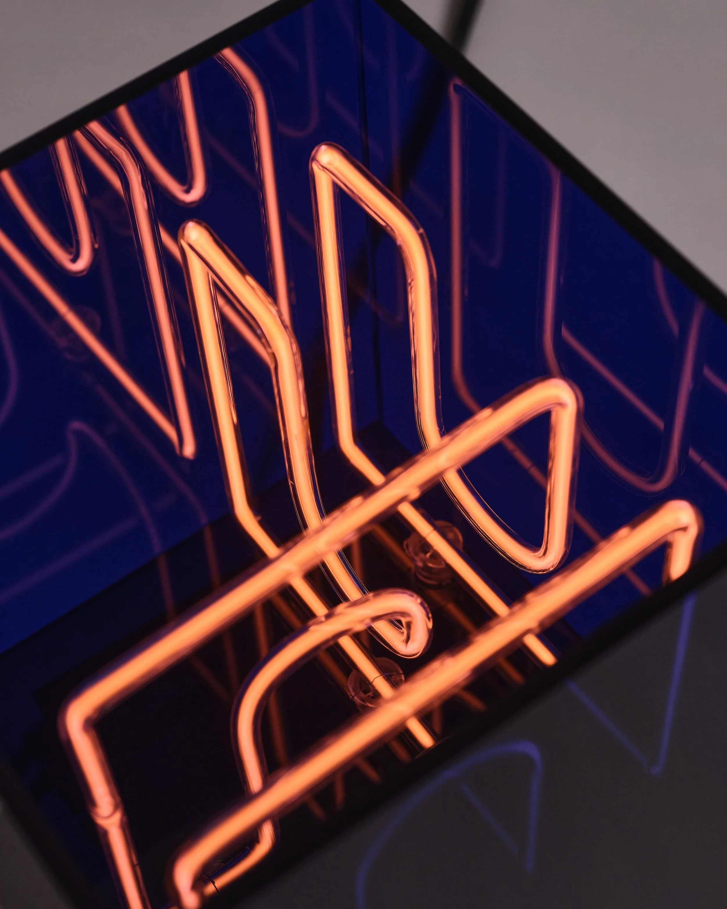 Close-up of an illuminated neon sculpture in orange reflected inside a blue acrylic box.