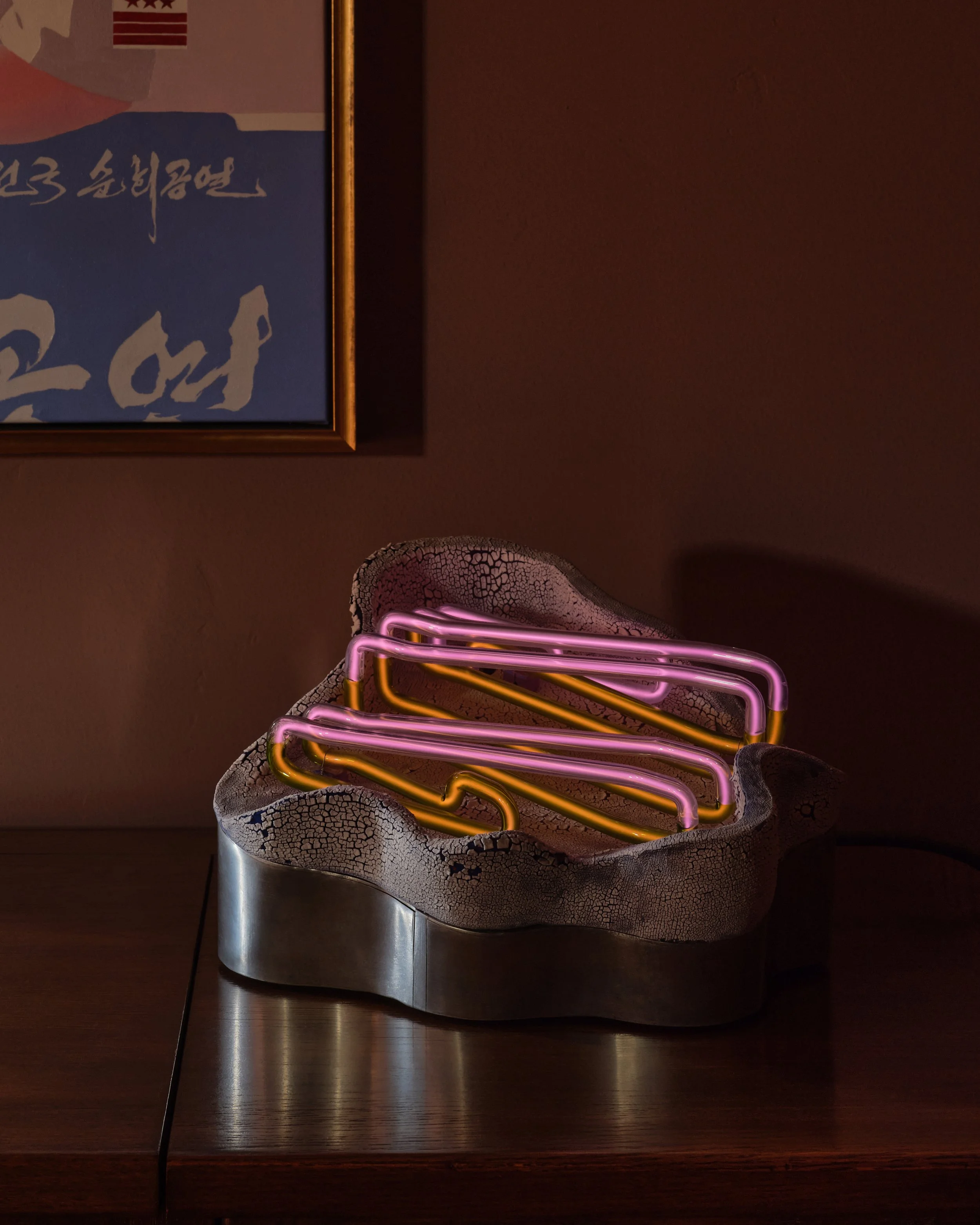 Neon light sculpture with pink and orange tubes in a rugged, cracked ceramic container on a wooden surface.