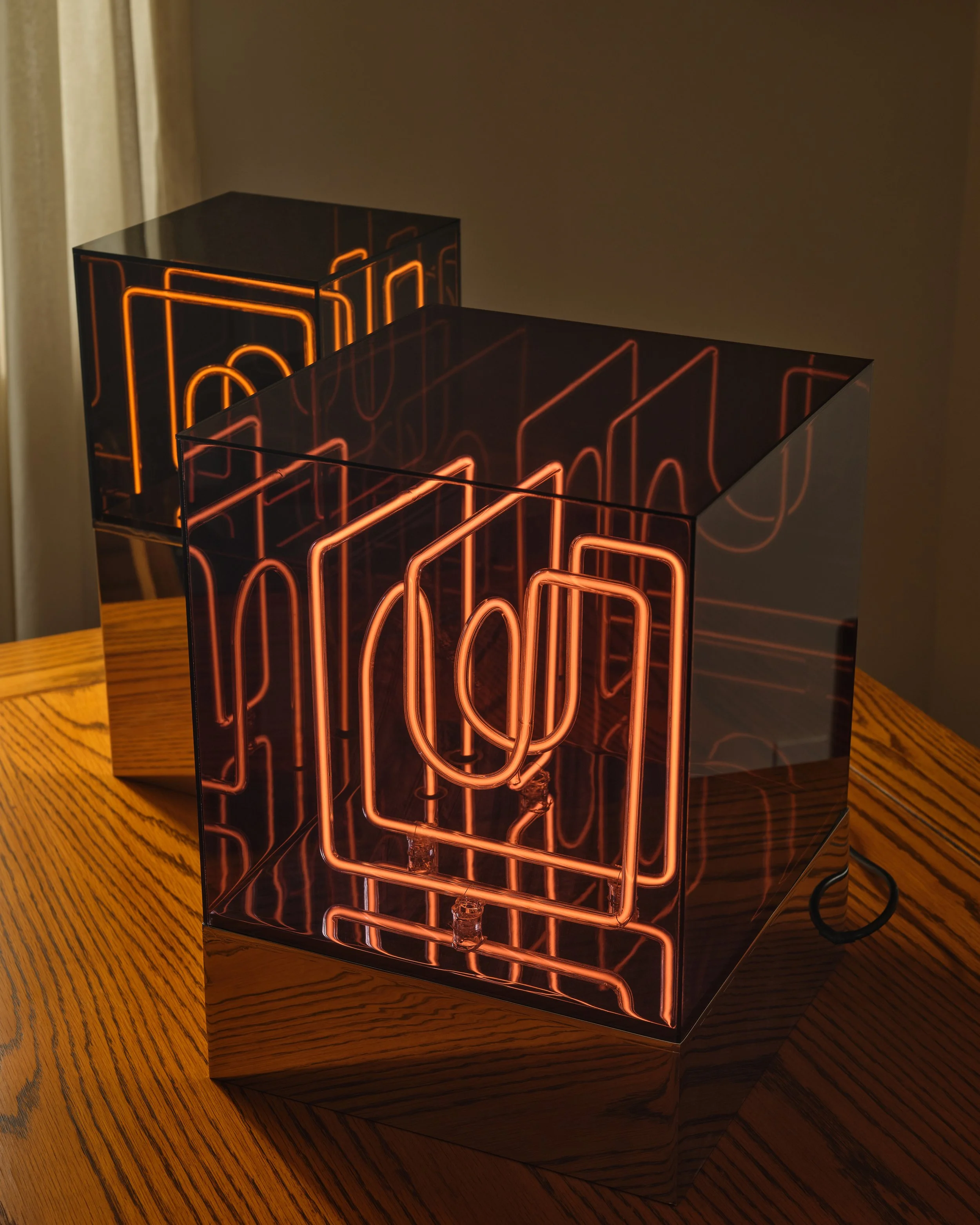 Decorative lamp with neon light design inside a transparent cube, placed on a wooden table.
