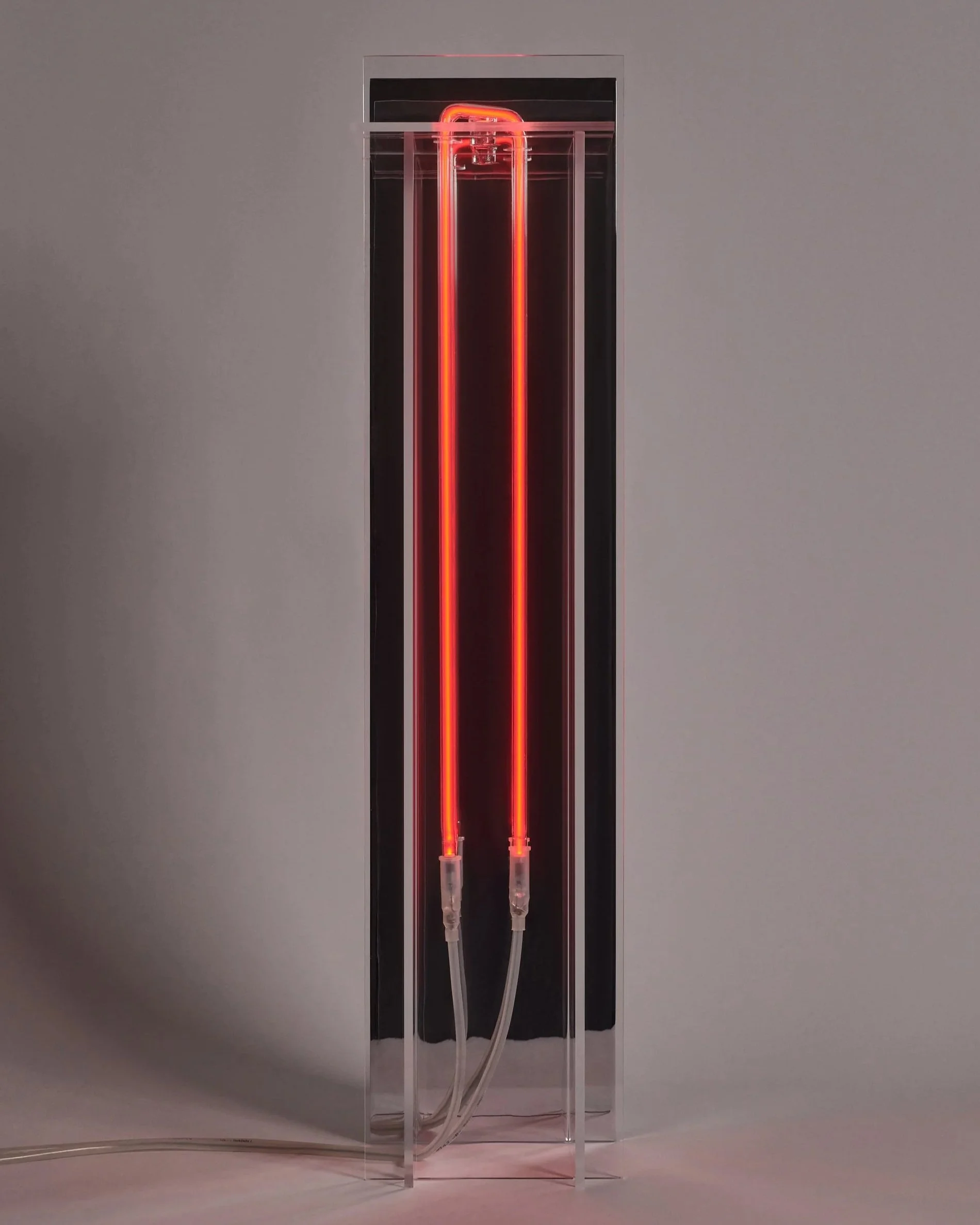 A neon red light sculpture with two neon tubes inside a glass case on a gray background.