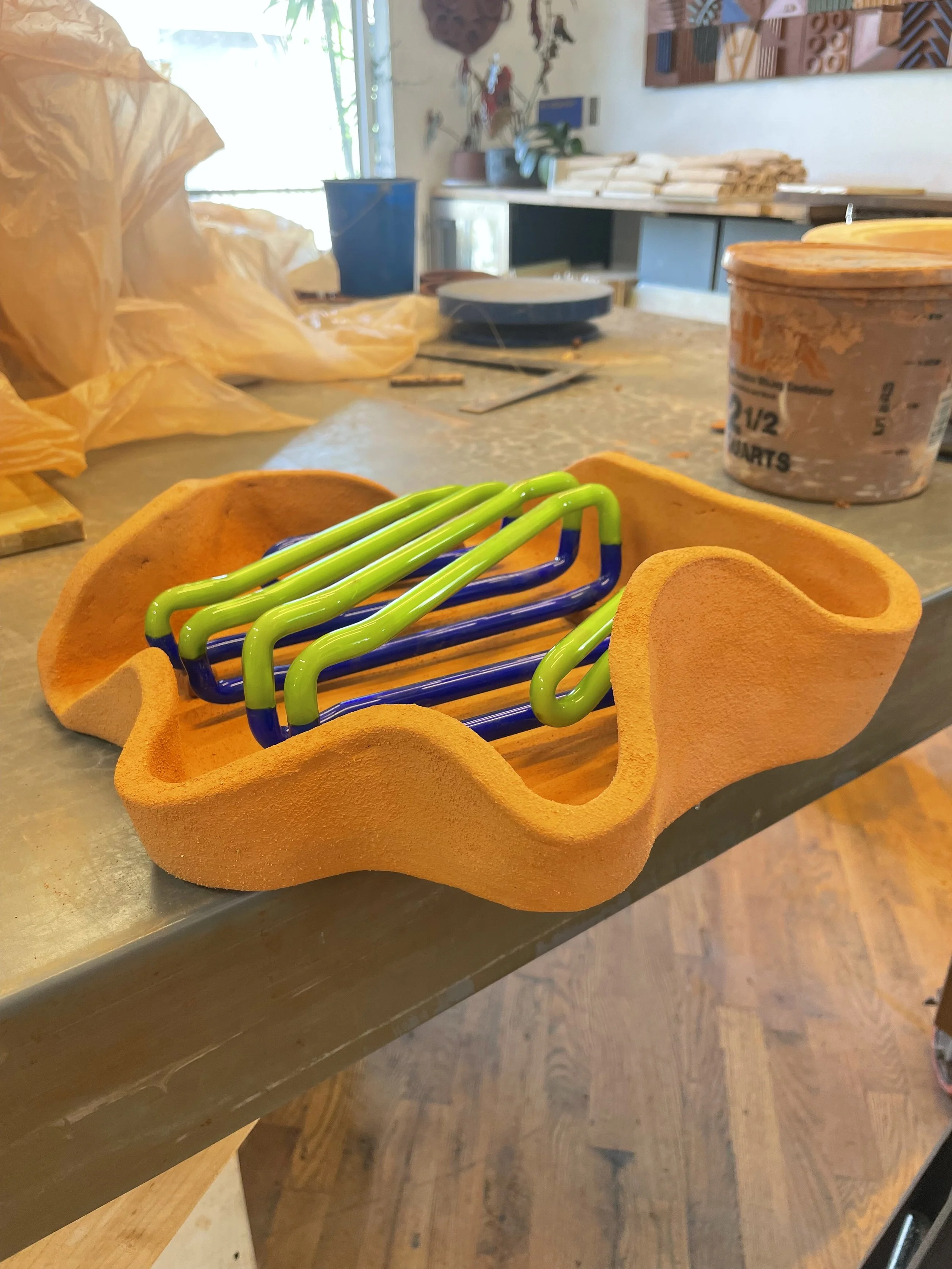 A foam tool tray with green and blue metal hooks inside it on a counter in an art studio, with art supplies and a window in the background.