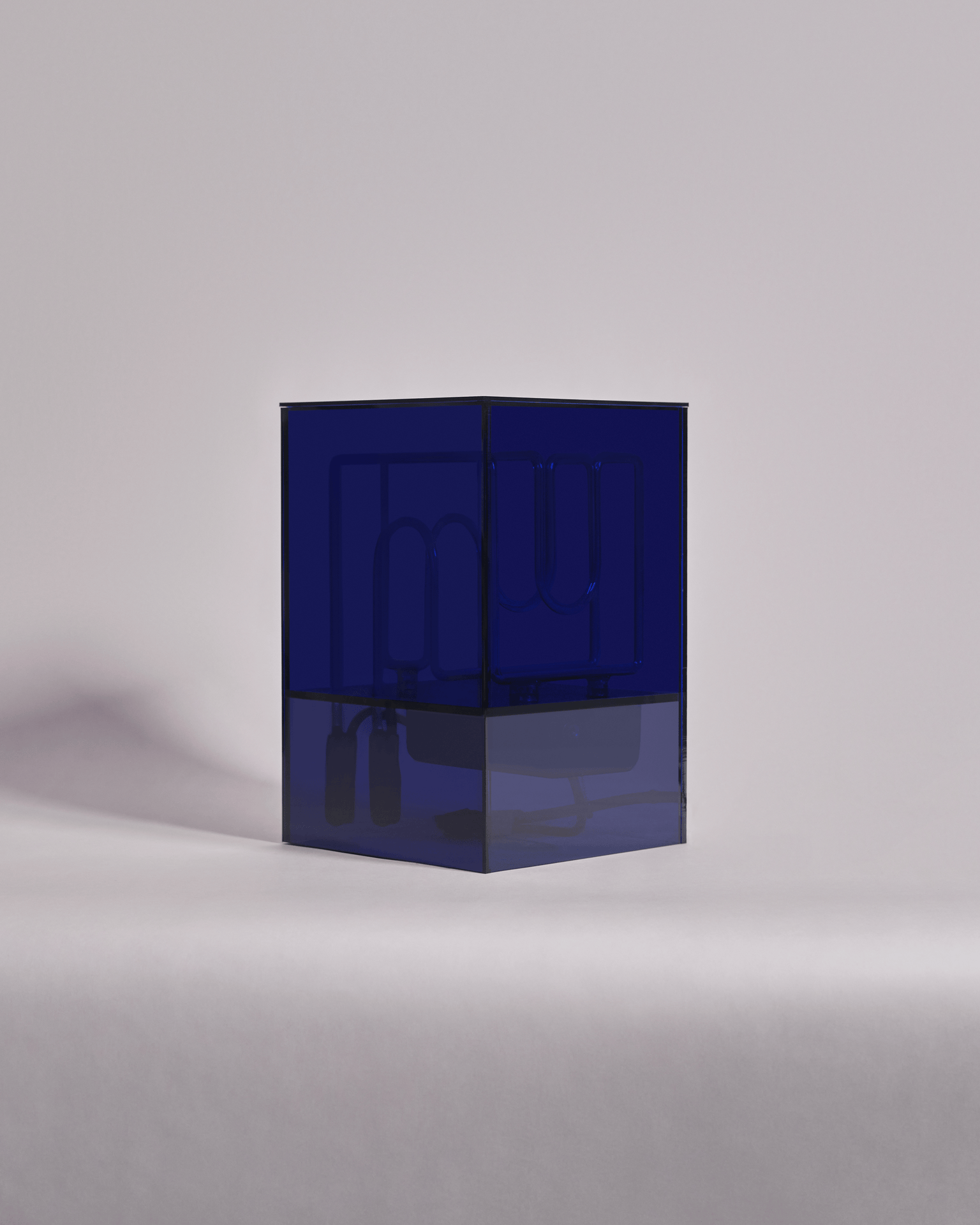 A transparent blue cube sculpture with internal neon tubing, placed on a white surface against a light gray background.