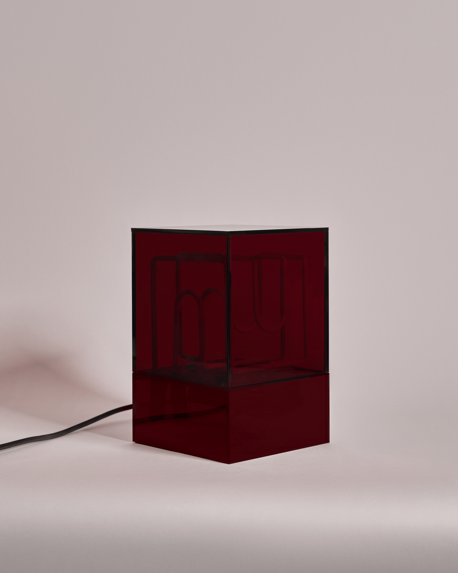 A modern lamp with a red, semi-transparent, rectangular shade with a black cord, placed on a plain surface.
