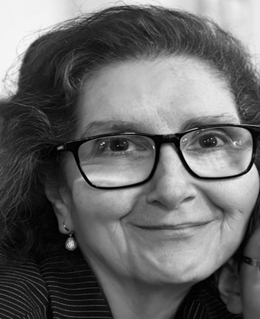 Close-up black and white portrait of a smiling woman with glasses, earrings, and wavy hair.