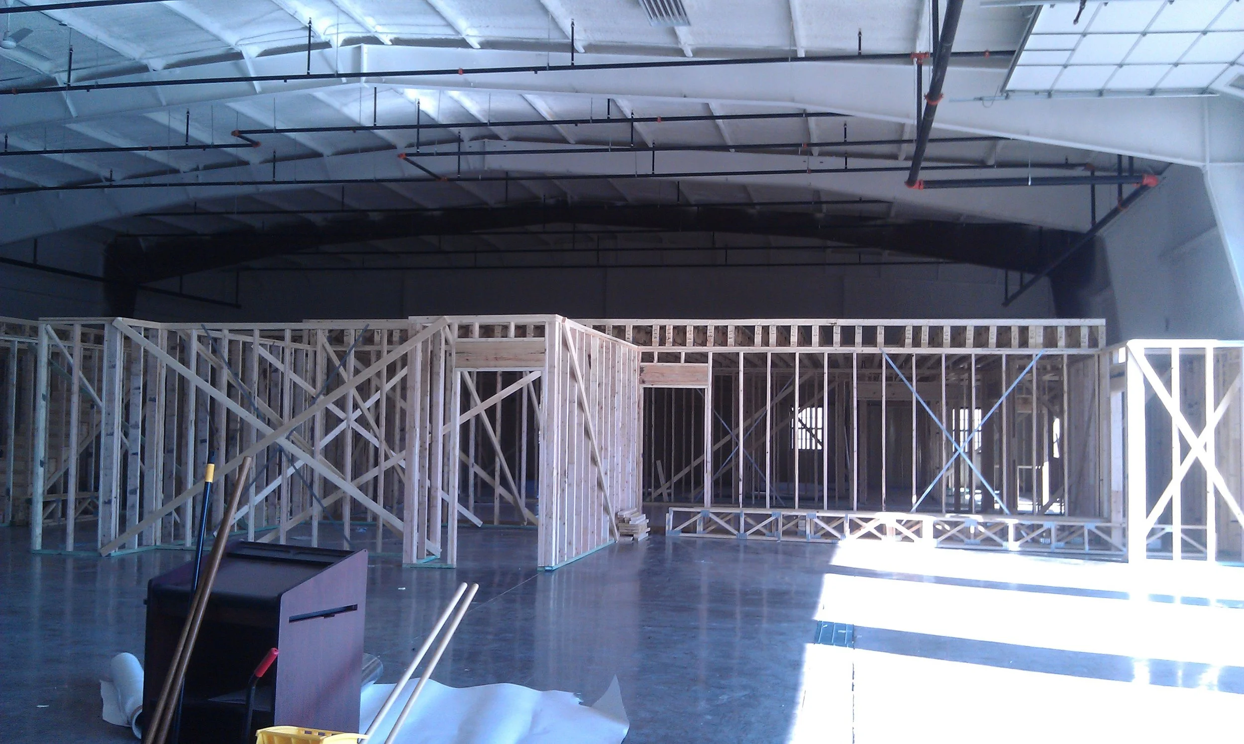 Interior view of a building under construction with exposed wooden framing and steel ceiling beams.
