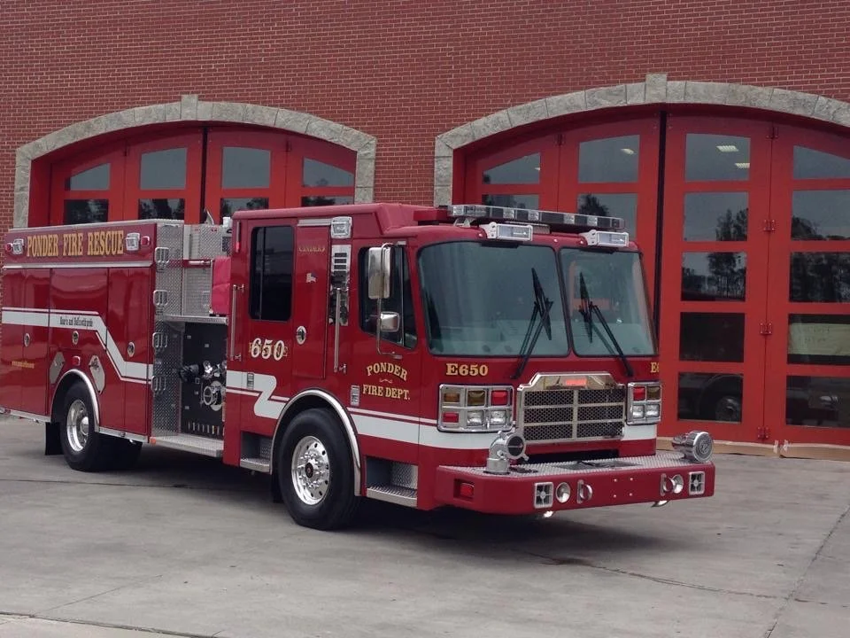 Red fire truck parked in front of a brick fire station with red doors.